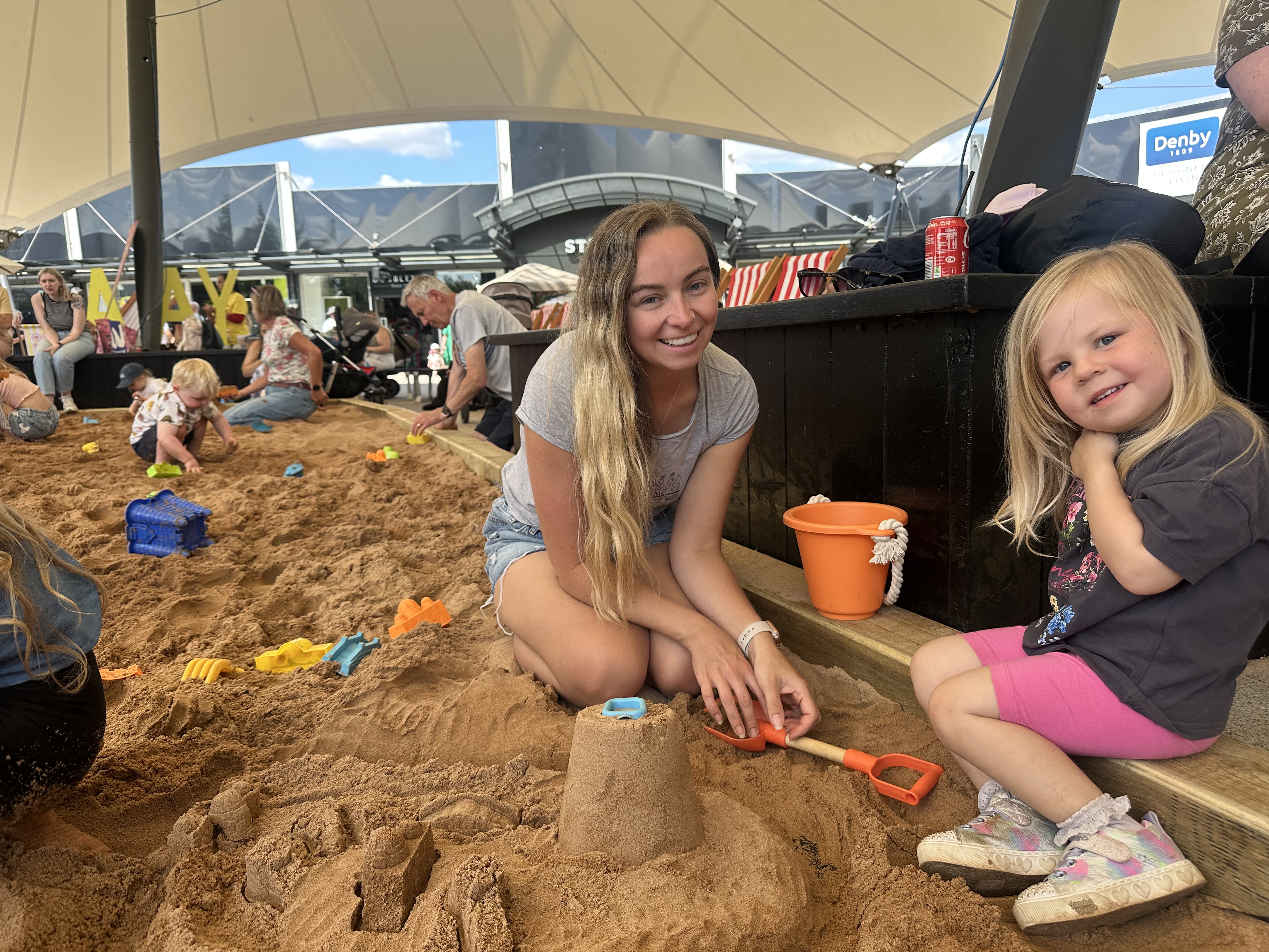 Children and adults enjoying a sandy play area under a canopy