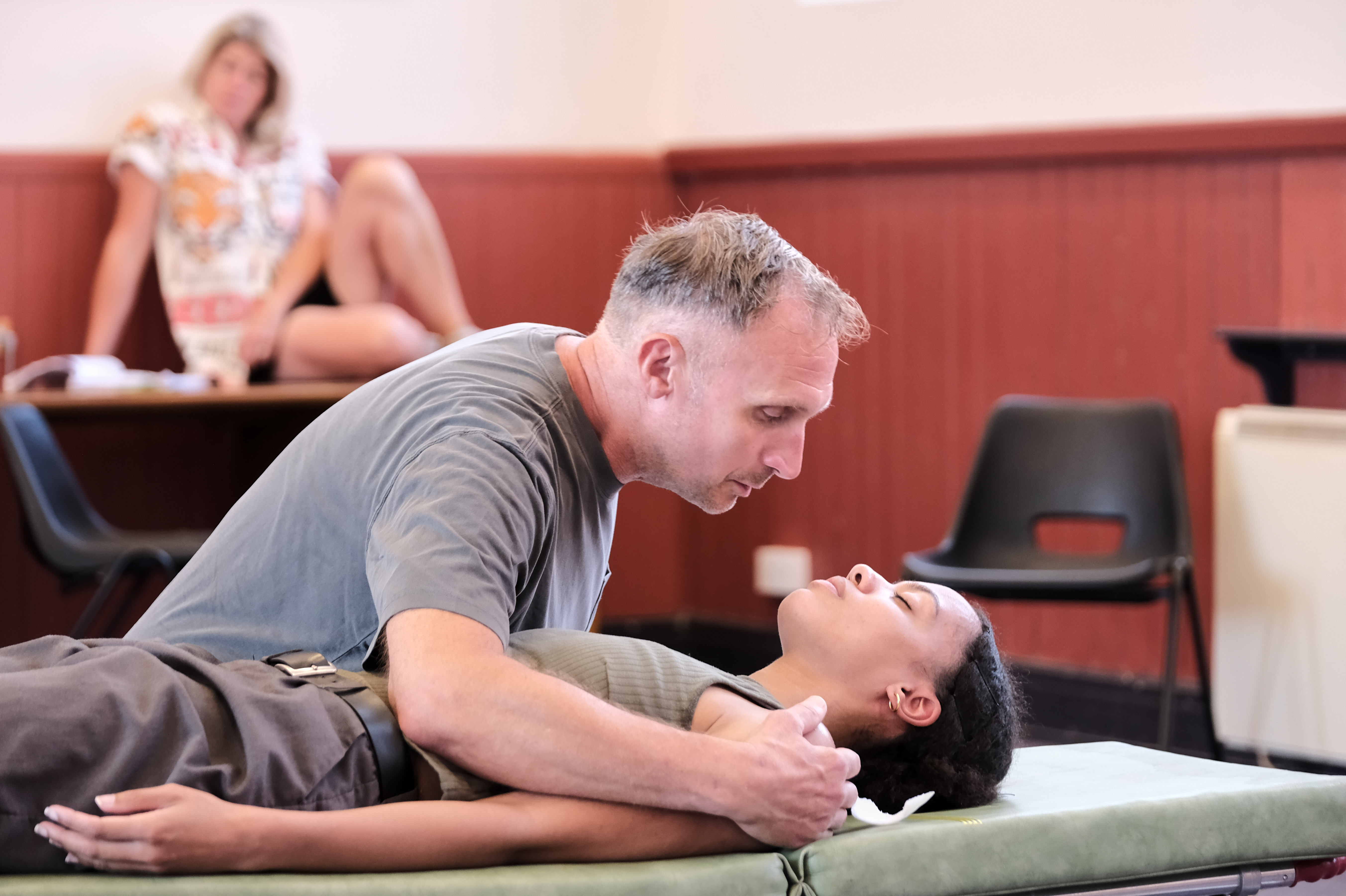 Man performing CPR on woman on a stretcher in a classroom