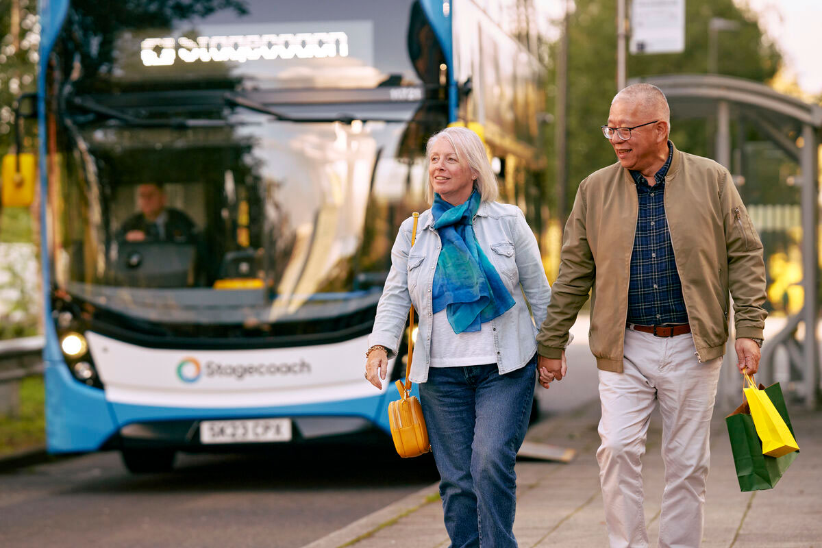 Smiling couple holding hands near a blue double-decker bus