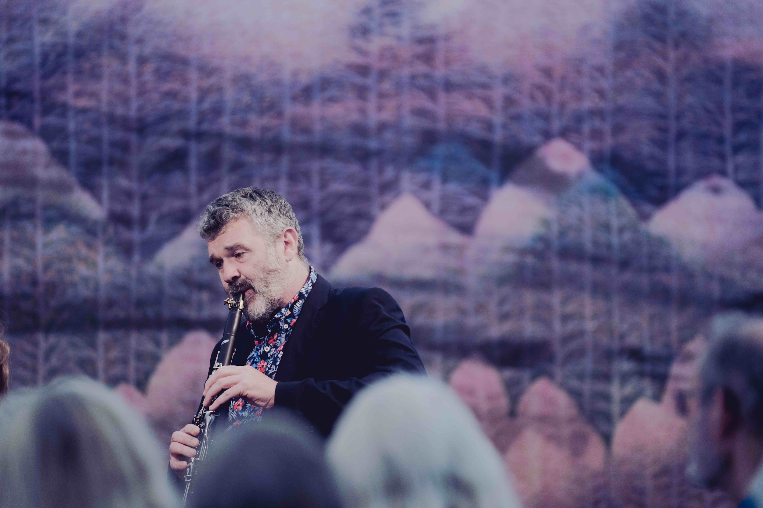 Man playing clarinet against a blurred mural backdrop