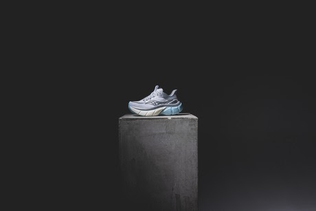 Modern grey trainer on concrete pedestal against dark background