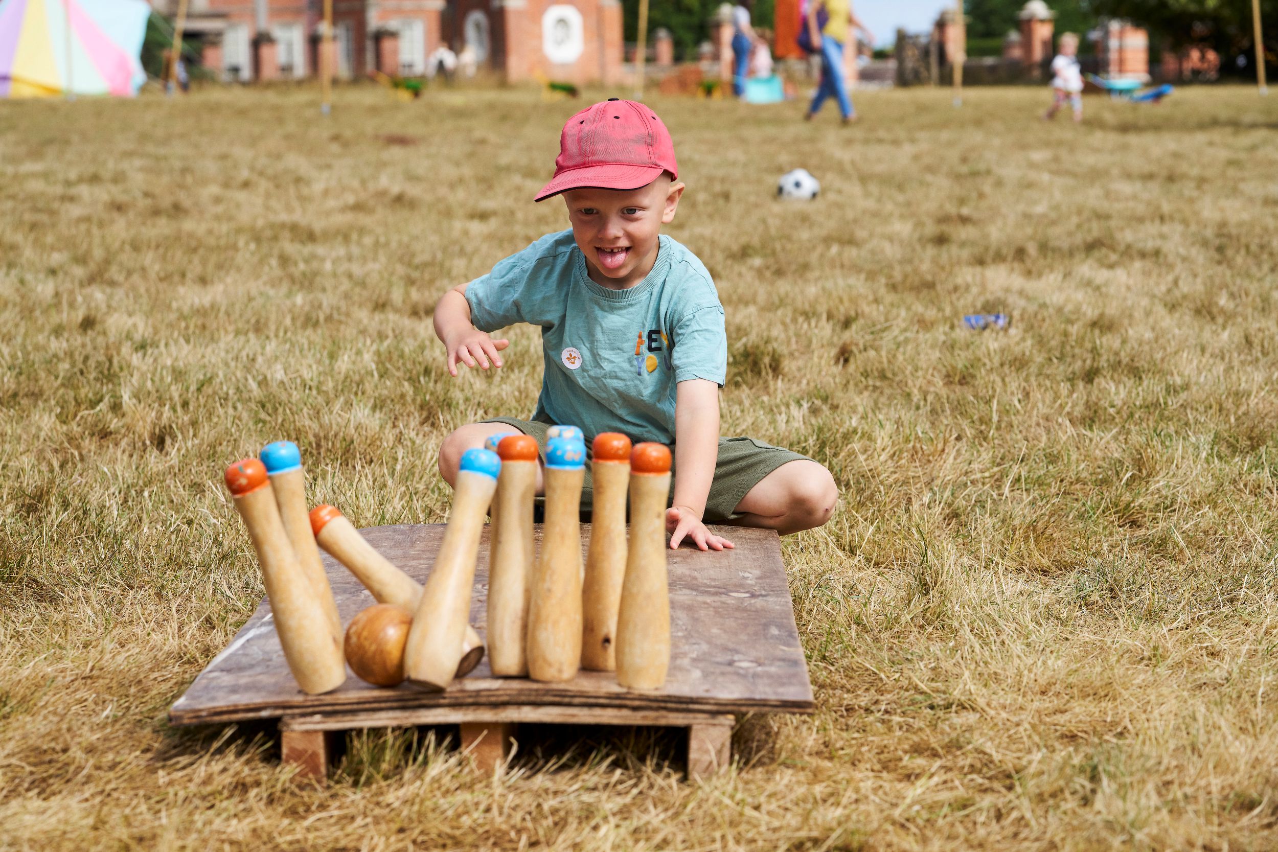 Child playing skittles on grassy field at summer fair