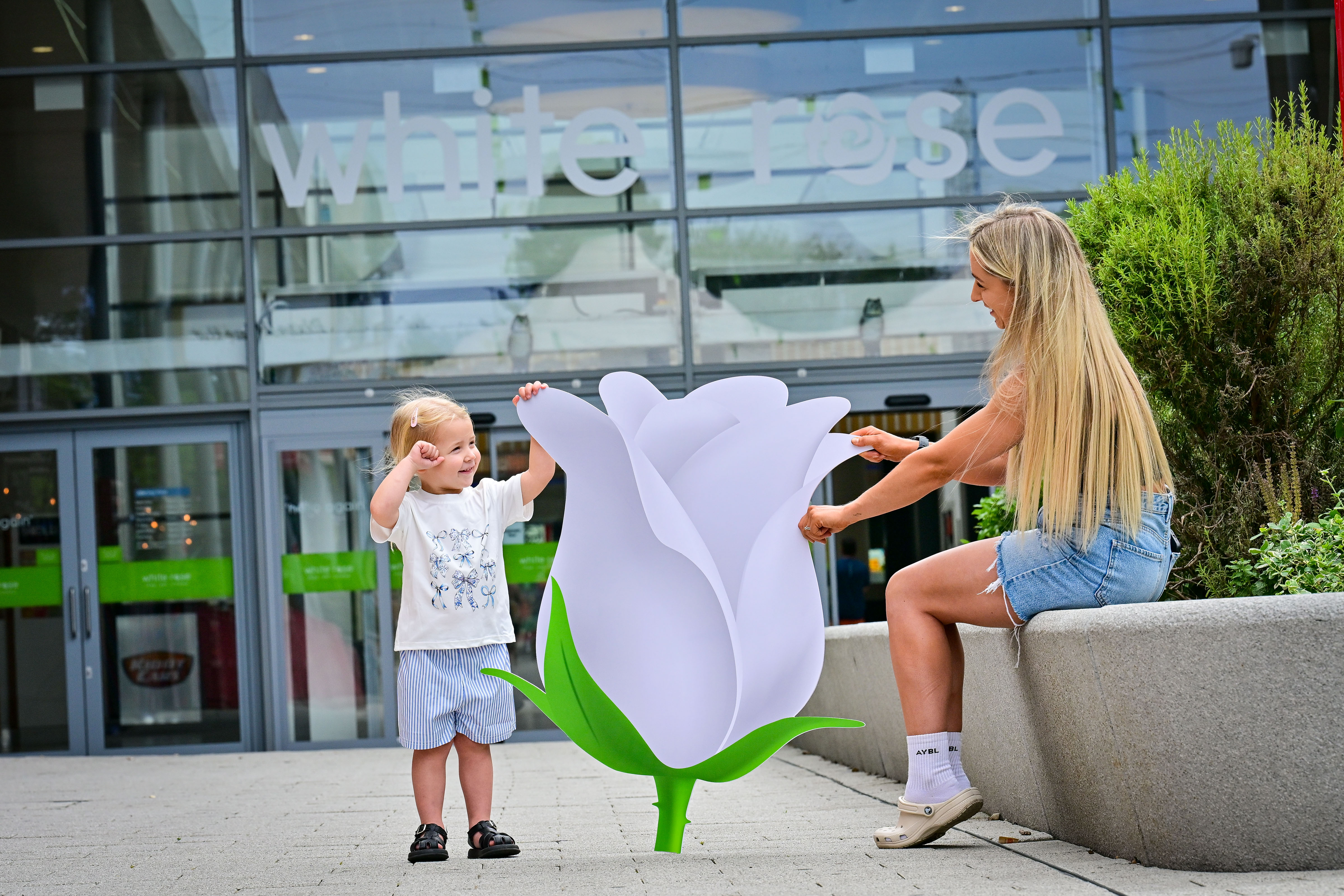 Child and woman interacting with giant white rose sculpture