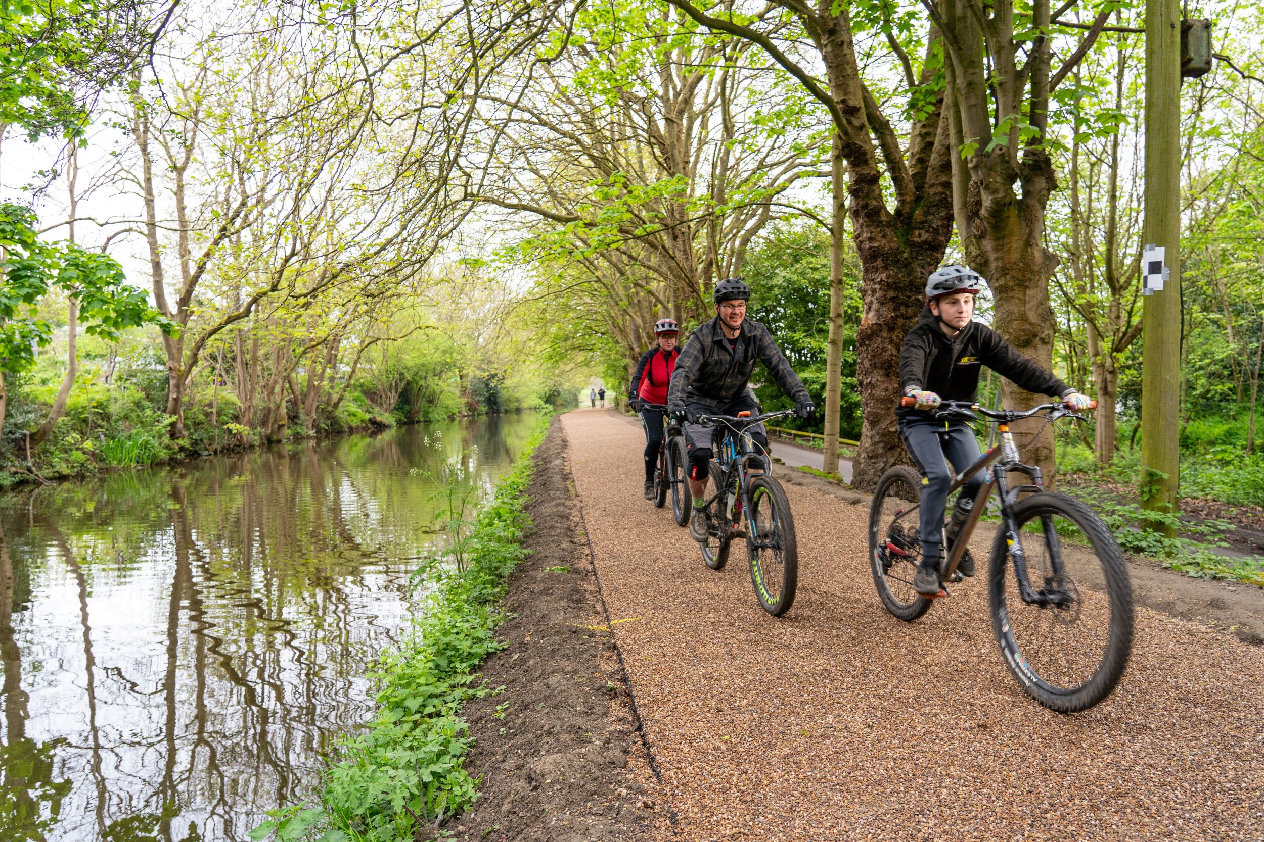 Cyclists riding on scenic path beside canal lined with trees