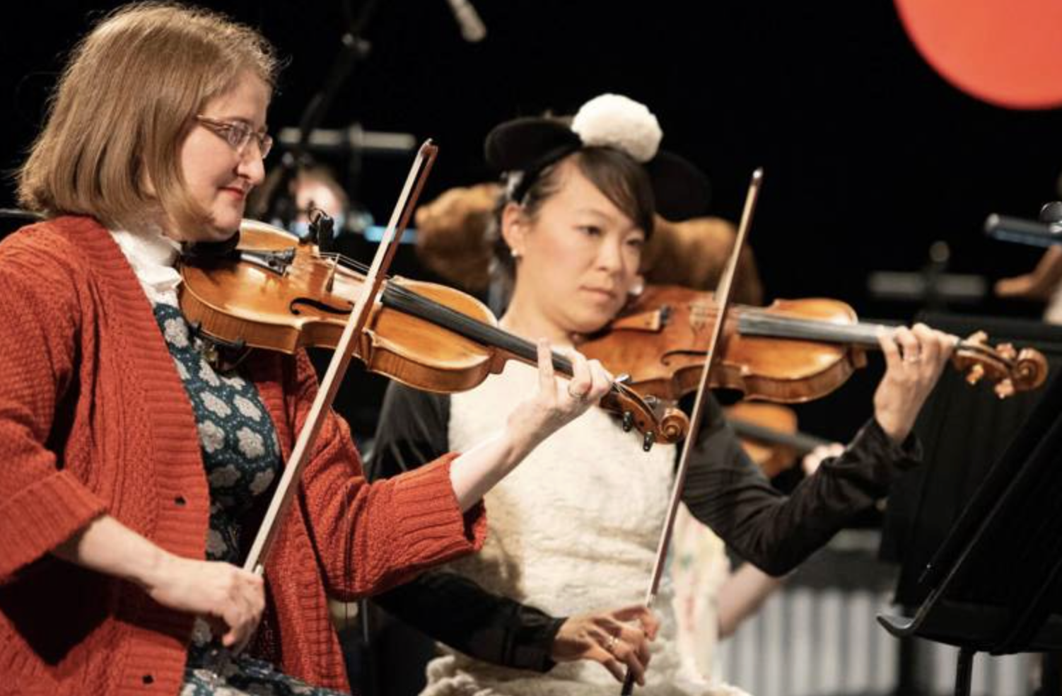 Two violinists, one in red sweater, one in costume, performing