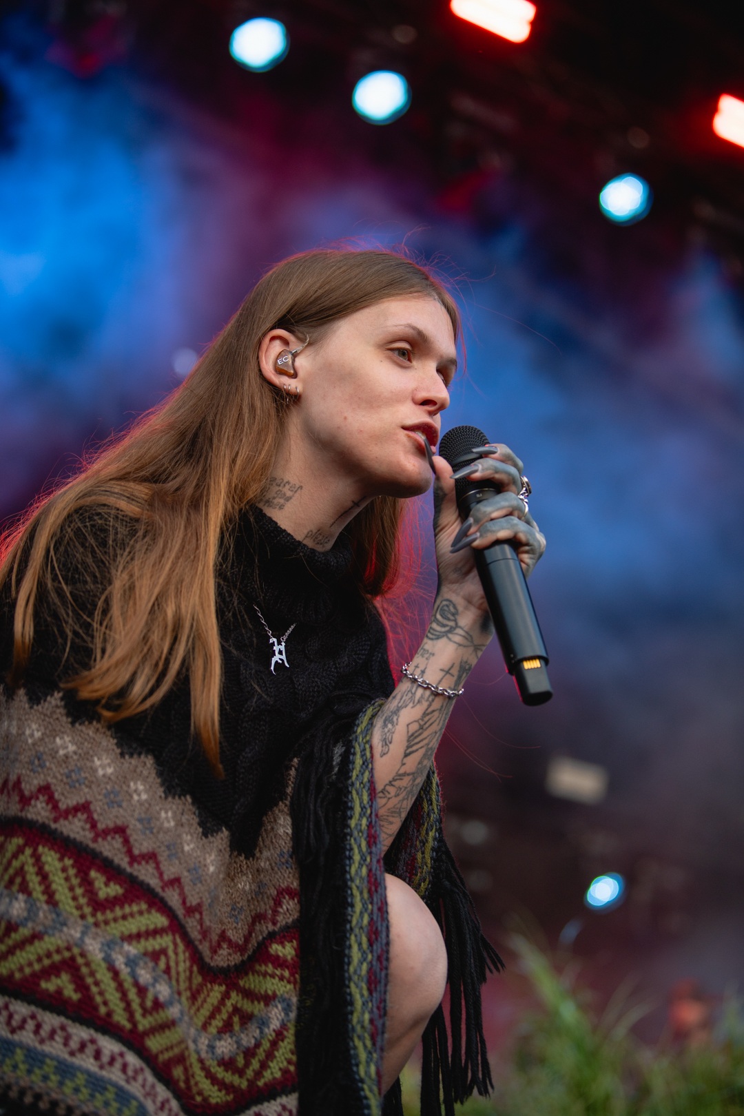 Singer with long hair performing on stage under colorful lights