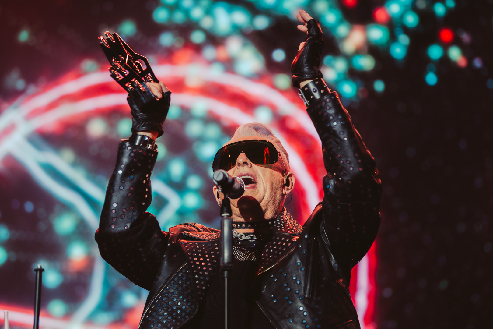 Performer in studded jacket and gloves on stage with vibrant lights
