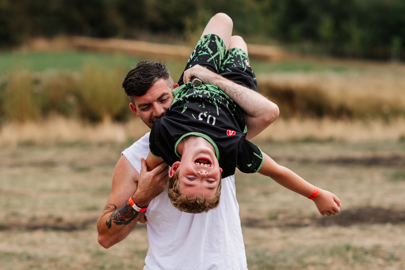 Man playfully holding laughing child upside down in grassy park