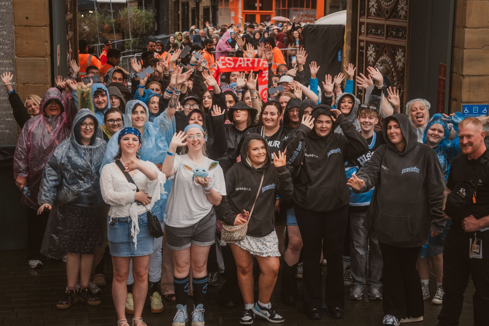 Cheerful crowd in raincoats waving outside historic building