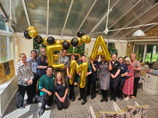 Group of people holding gold balloons in a sunlit room