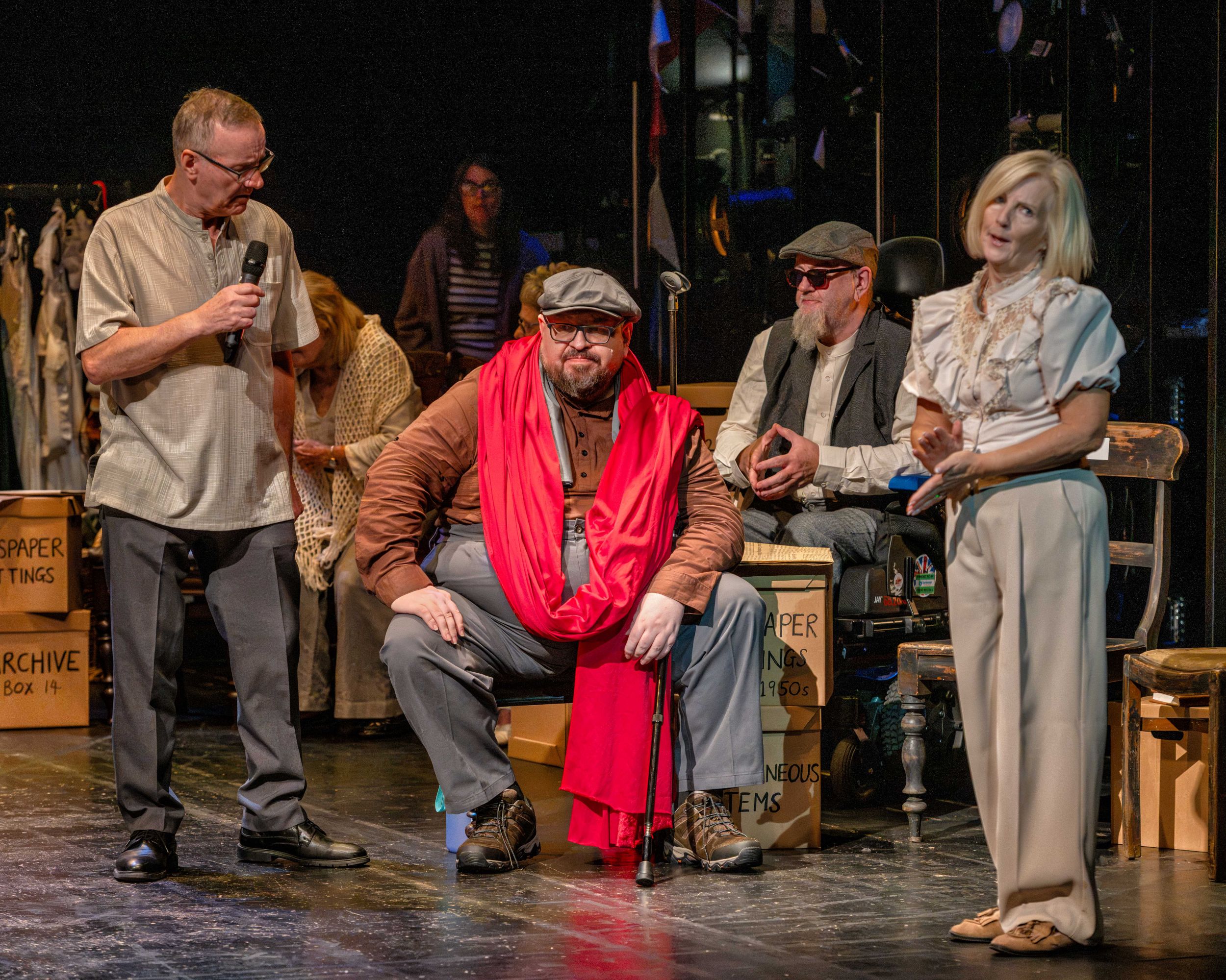 Group of actors in a theatre, one wearing a red scarf and cap