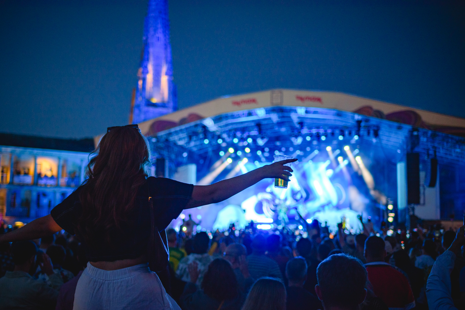 Crowd enjoying a concert at night with lit stage and spire