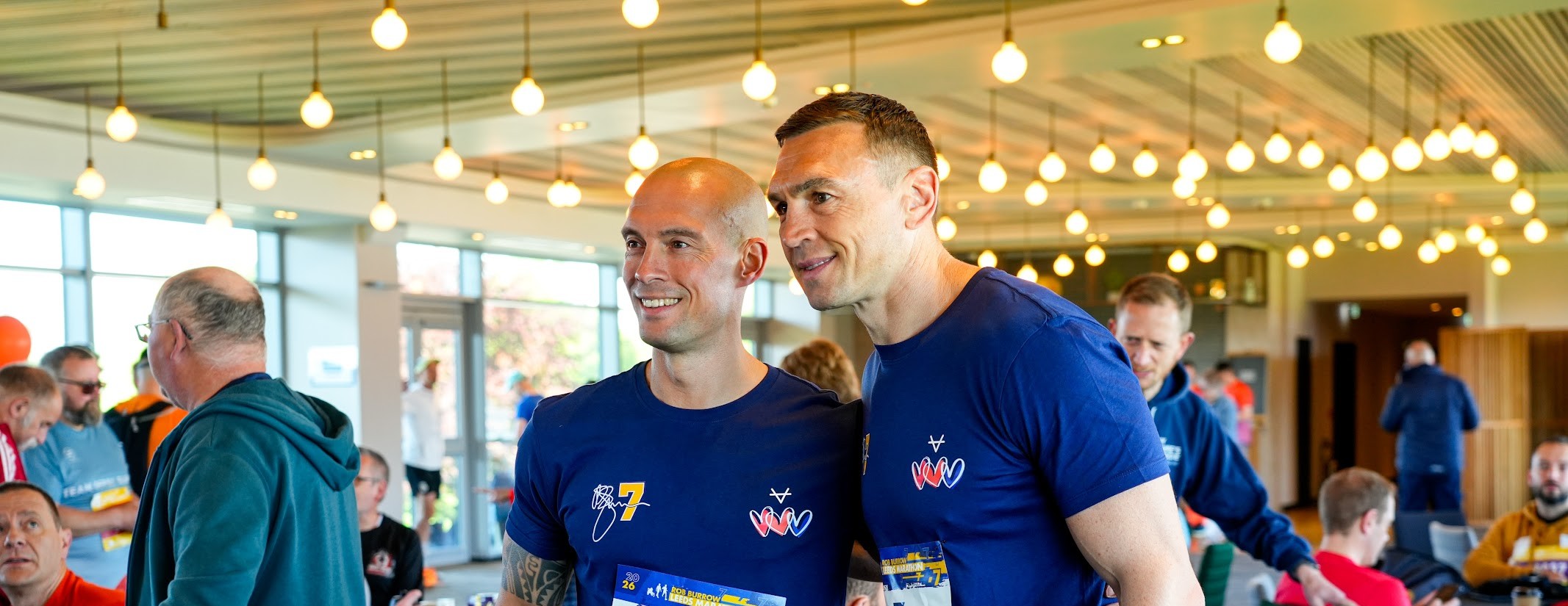 Two men in blue shirts at a lively indoor event with hanging lights