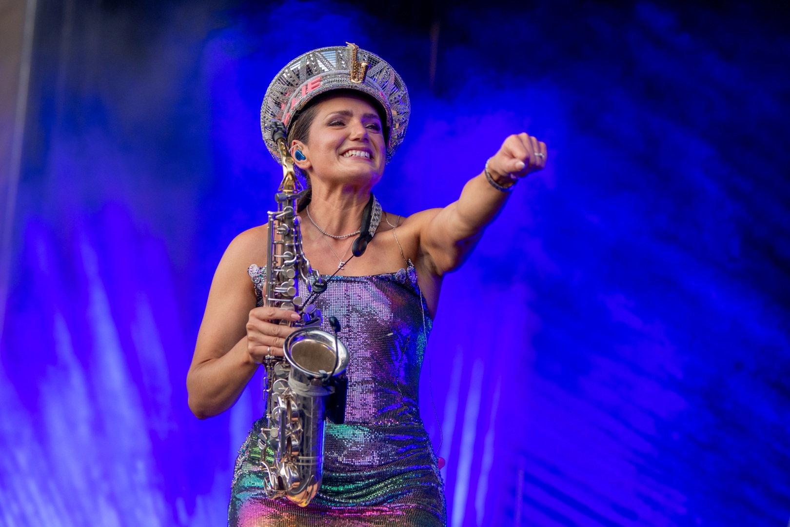 Musician in sparkly dress and hat playing saxophone on stage