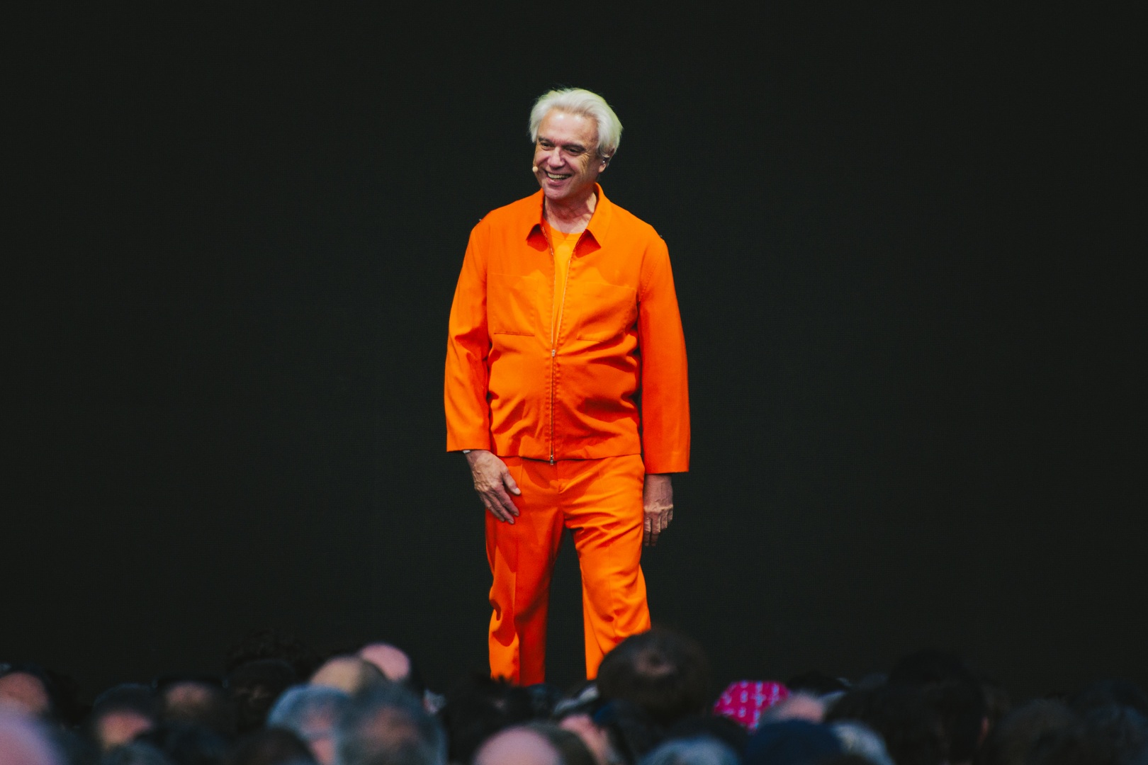 Person in bright orange suit stands smiling against black background