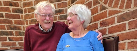Elderly couple smiling and sitting against a brick wall