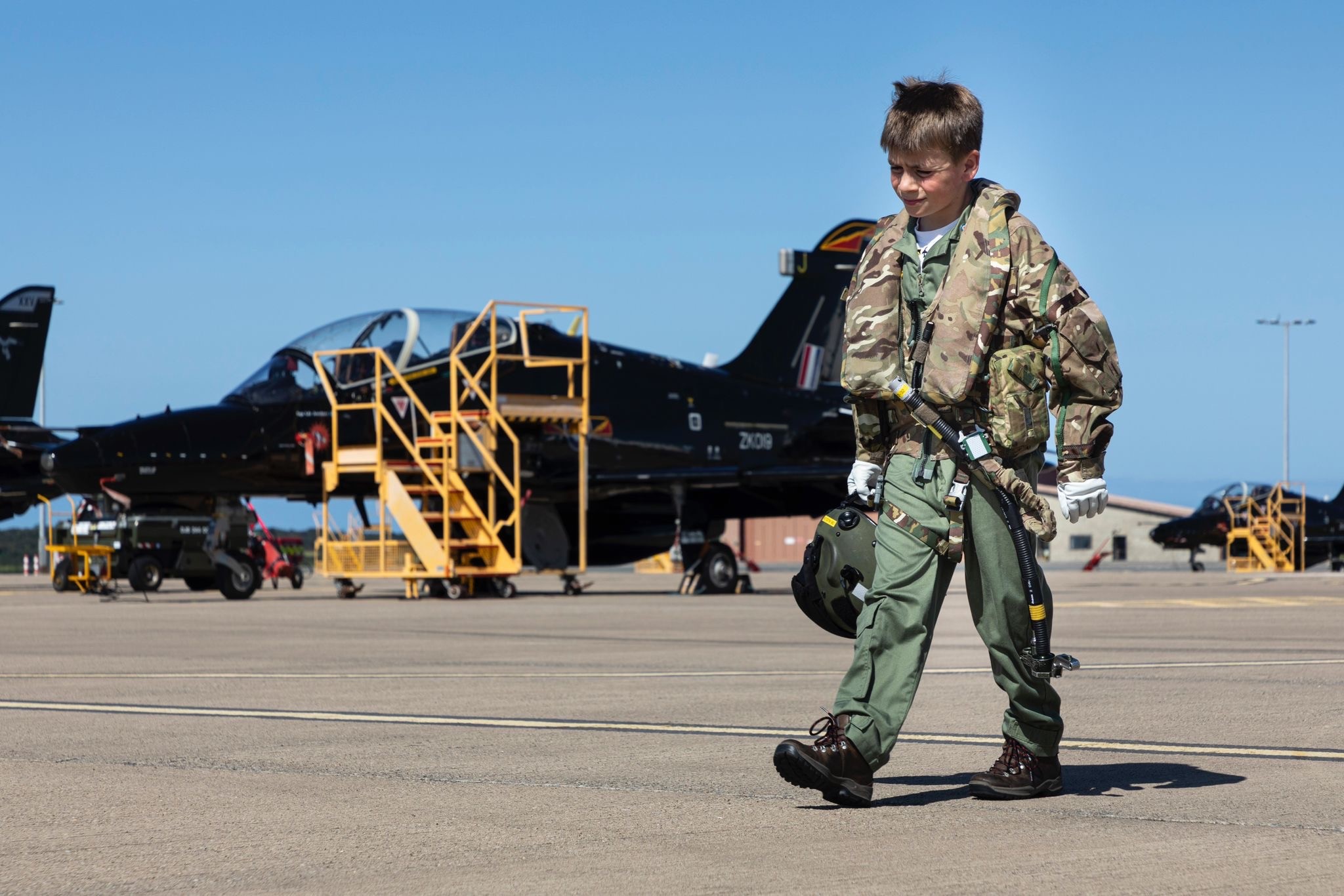 Young boy in pilot uniform walking on airfield near jets