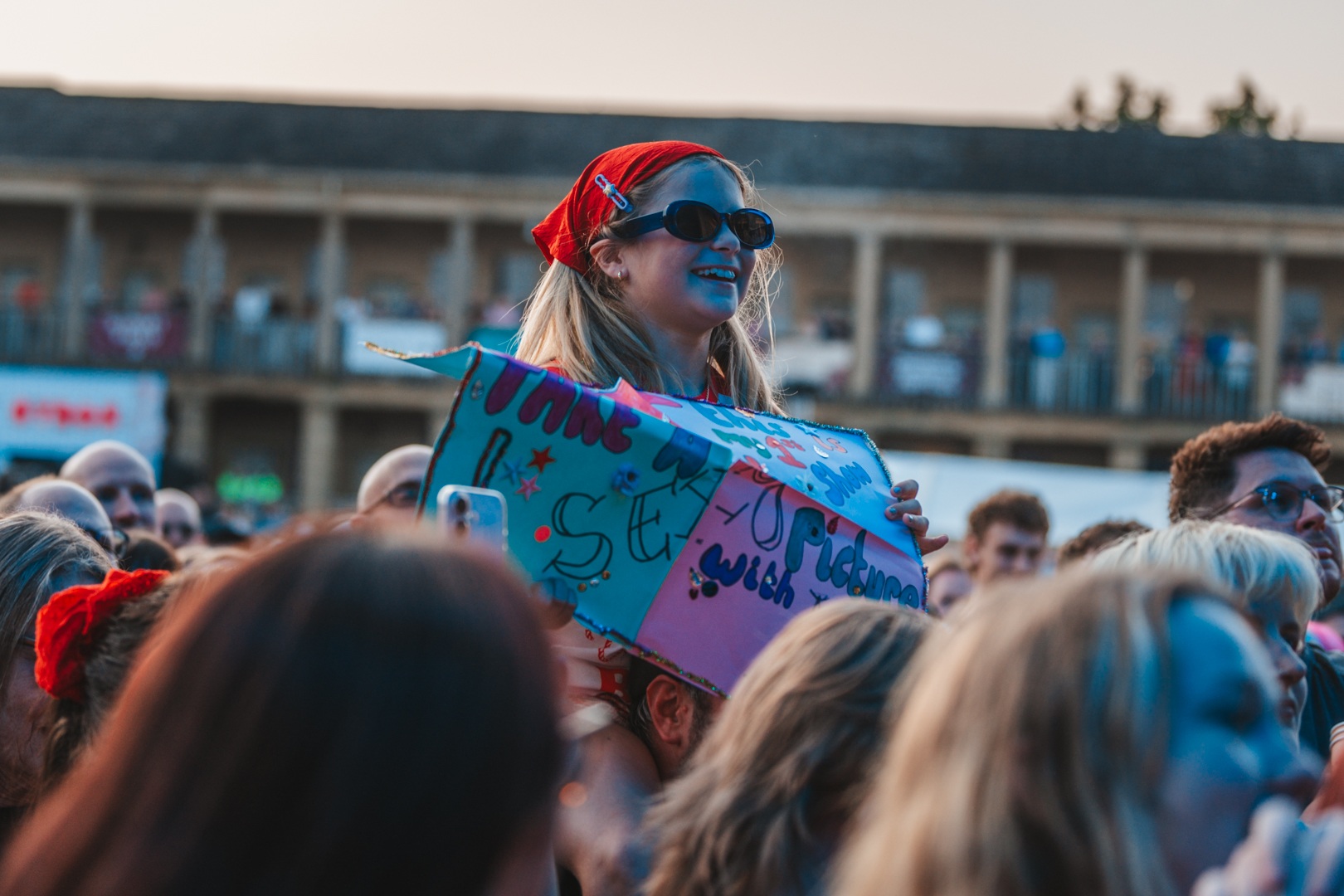 Festival crowd at sunset with woman holding colourful sign