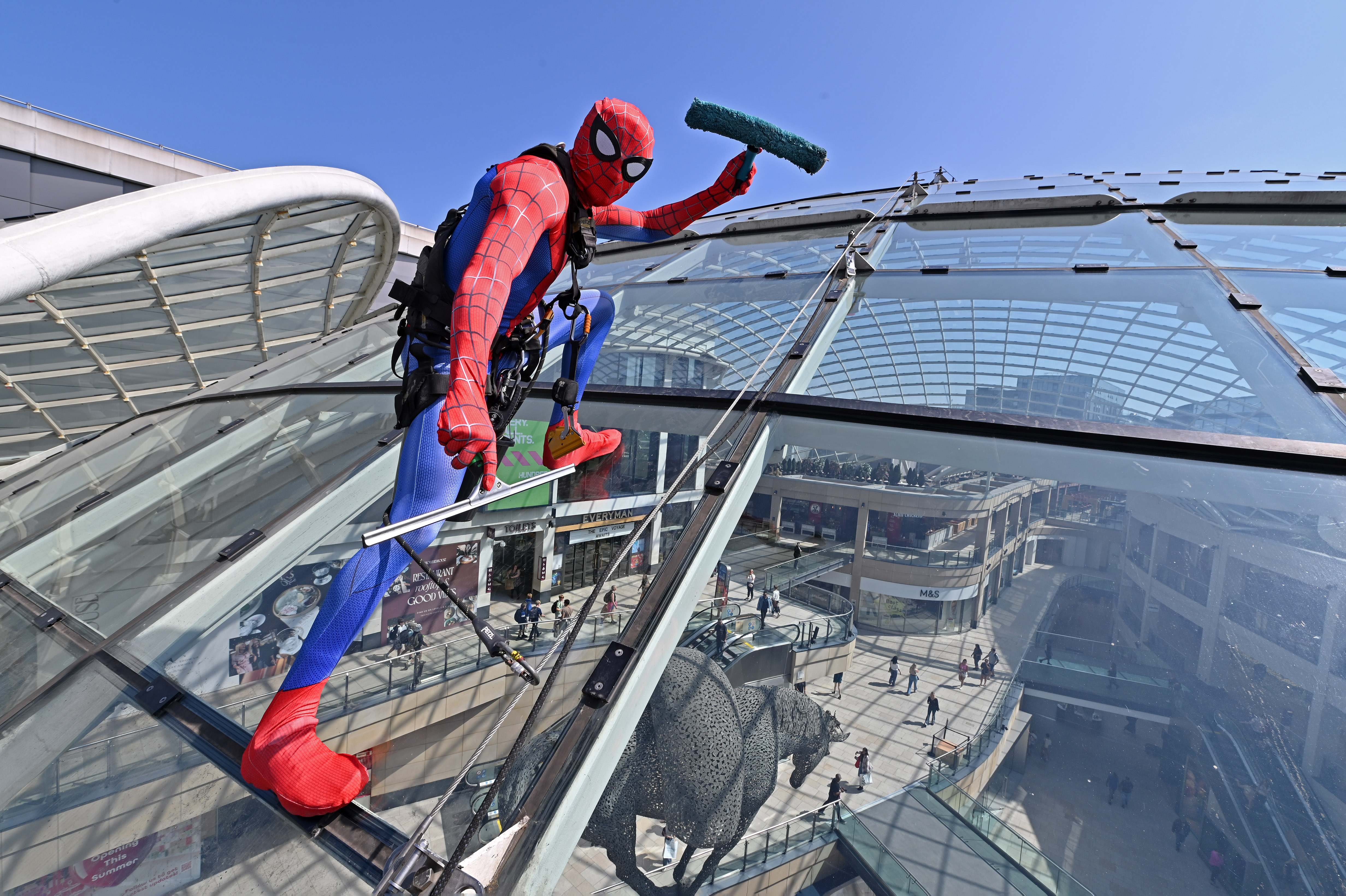 Person in superhero costume cleaning glass roof of shopping centre