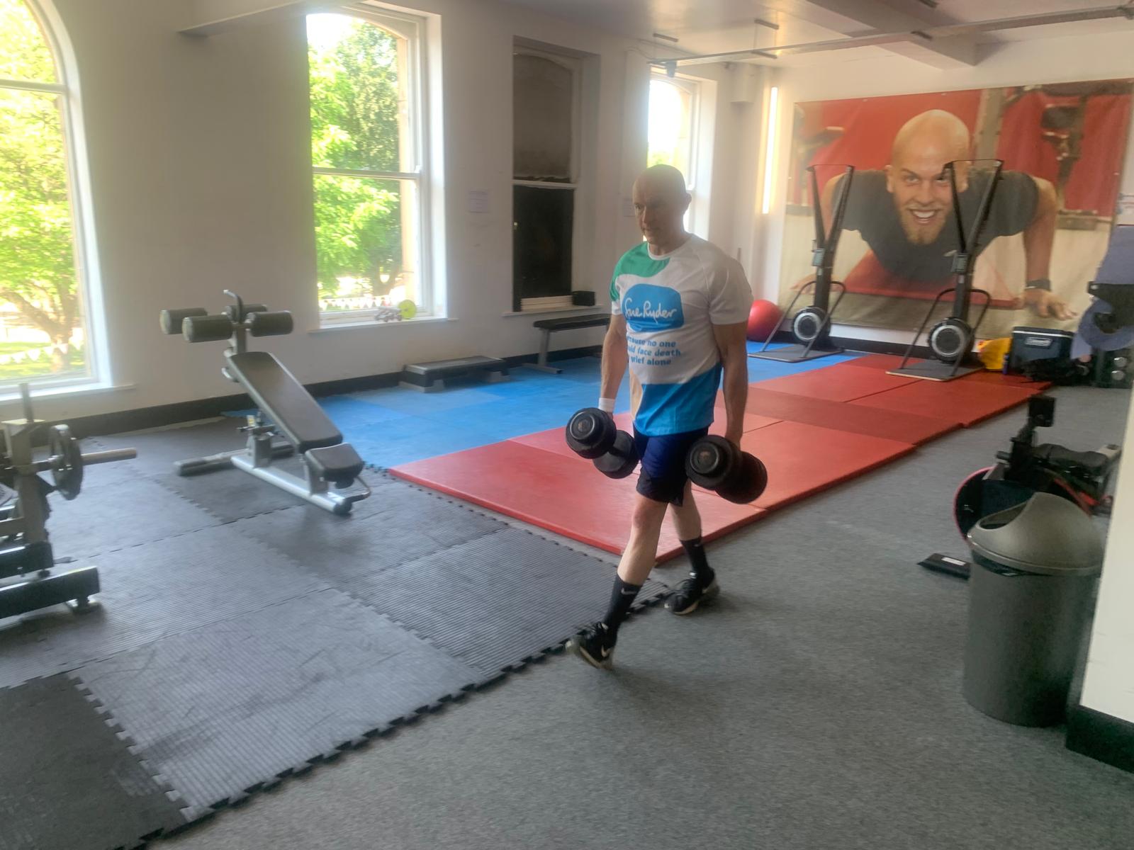 Man lifting weights in a brightly lit gym with large windows