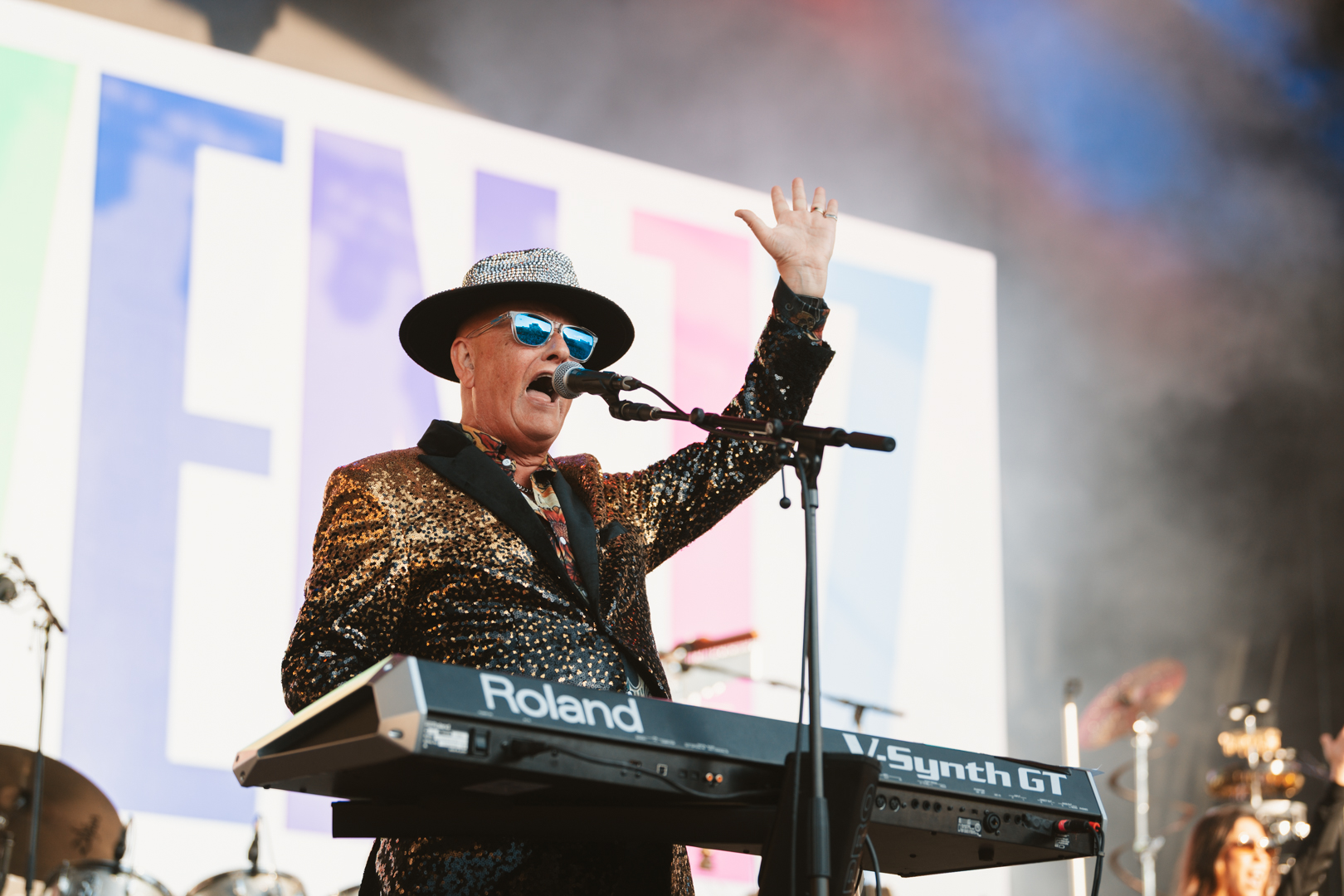 Musician in sequined jacket and hat performing on keyboard