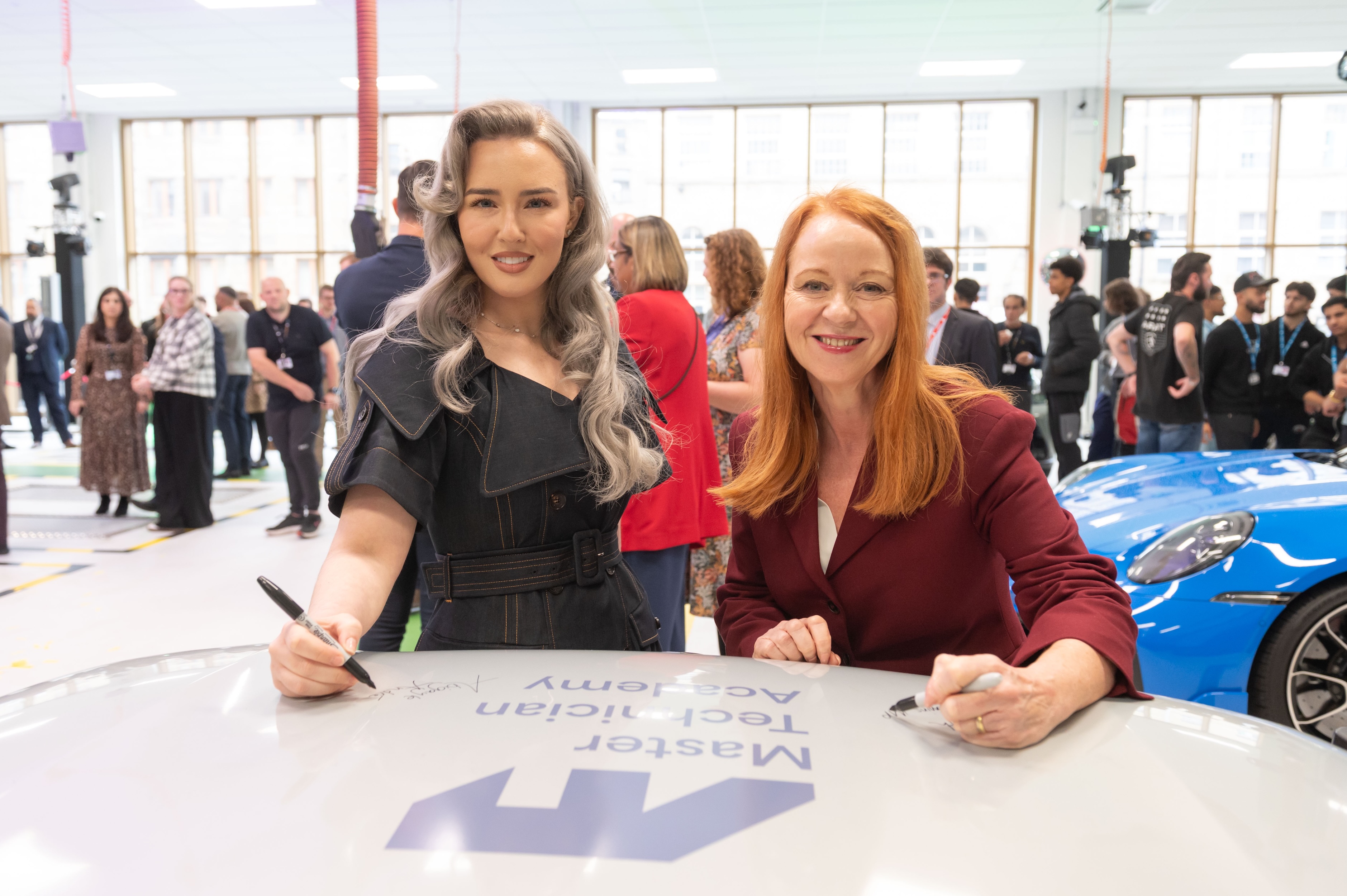 Two women signing a car bonnet at a technology event
