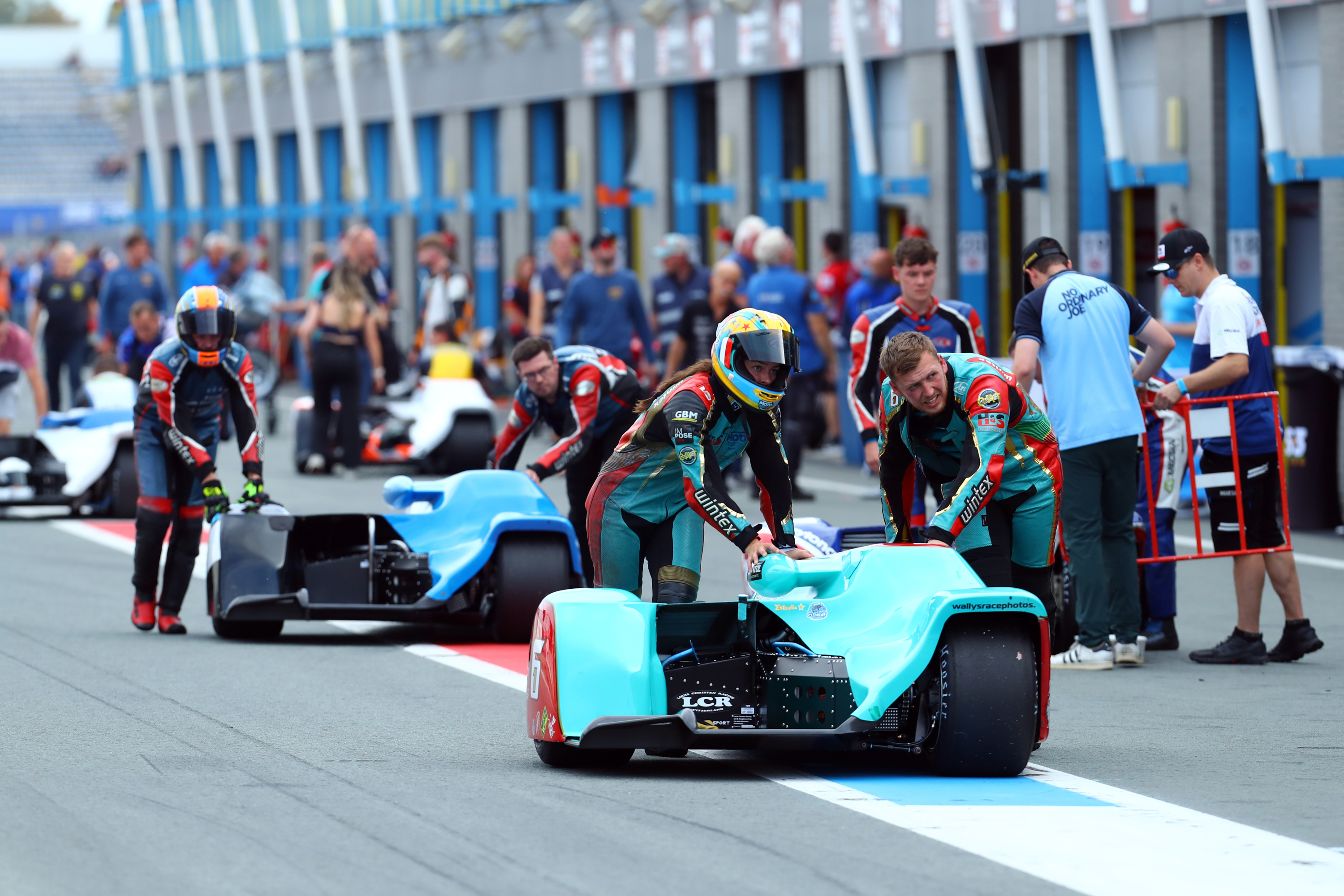 Racers preparing sidecar motorcycles on a track with pit garages