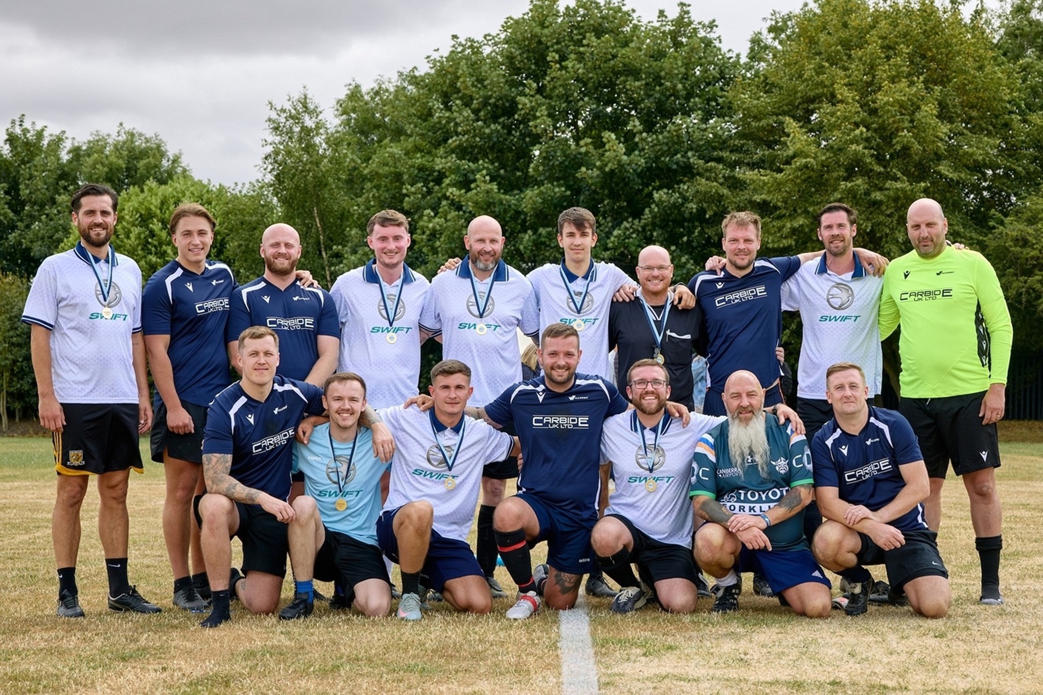 Group of smiling footballers with medals on grassy pitch