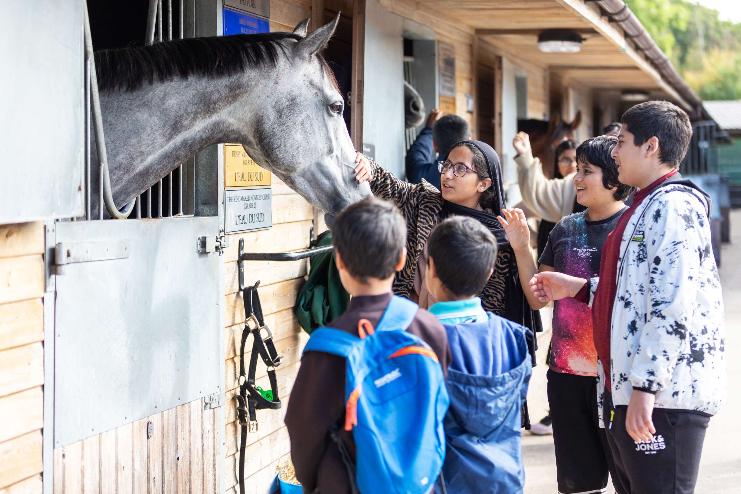 Children petting a grey horse in a wooden stable at a farm