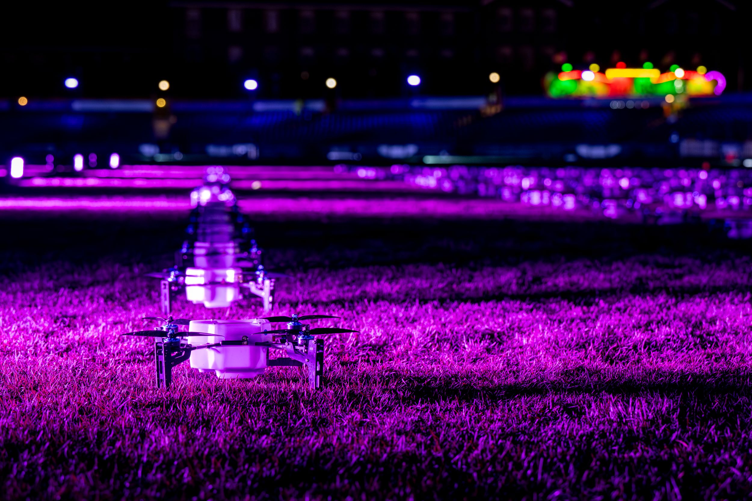 Illuminated drones in vibrant purple lights on a grassy field