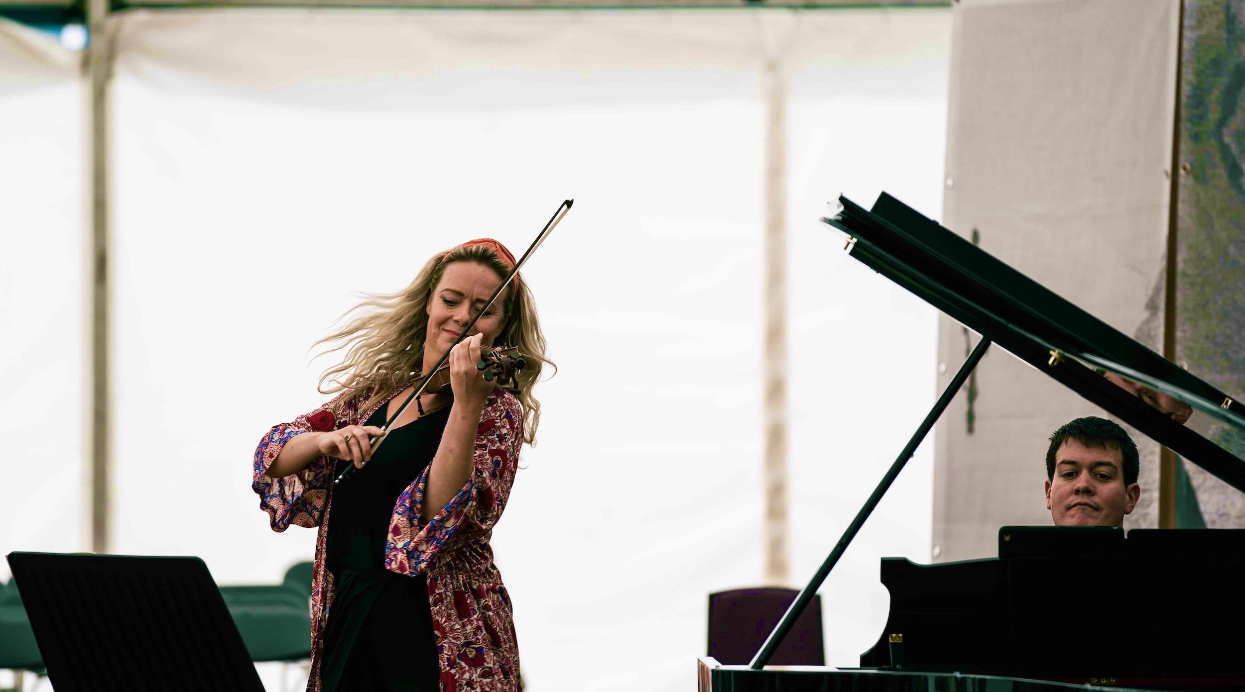 Woman playing violin near grand piano in a bright tent