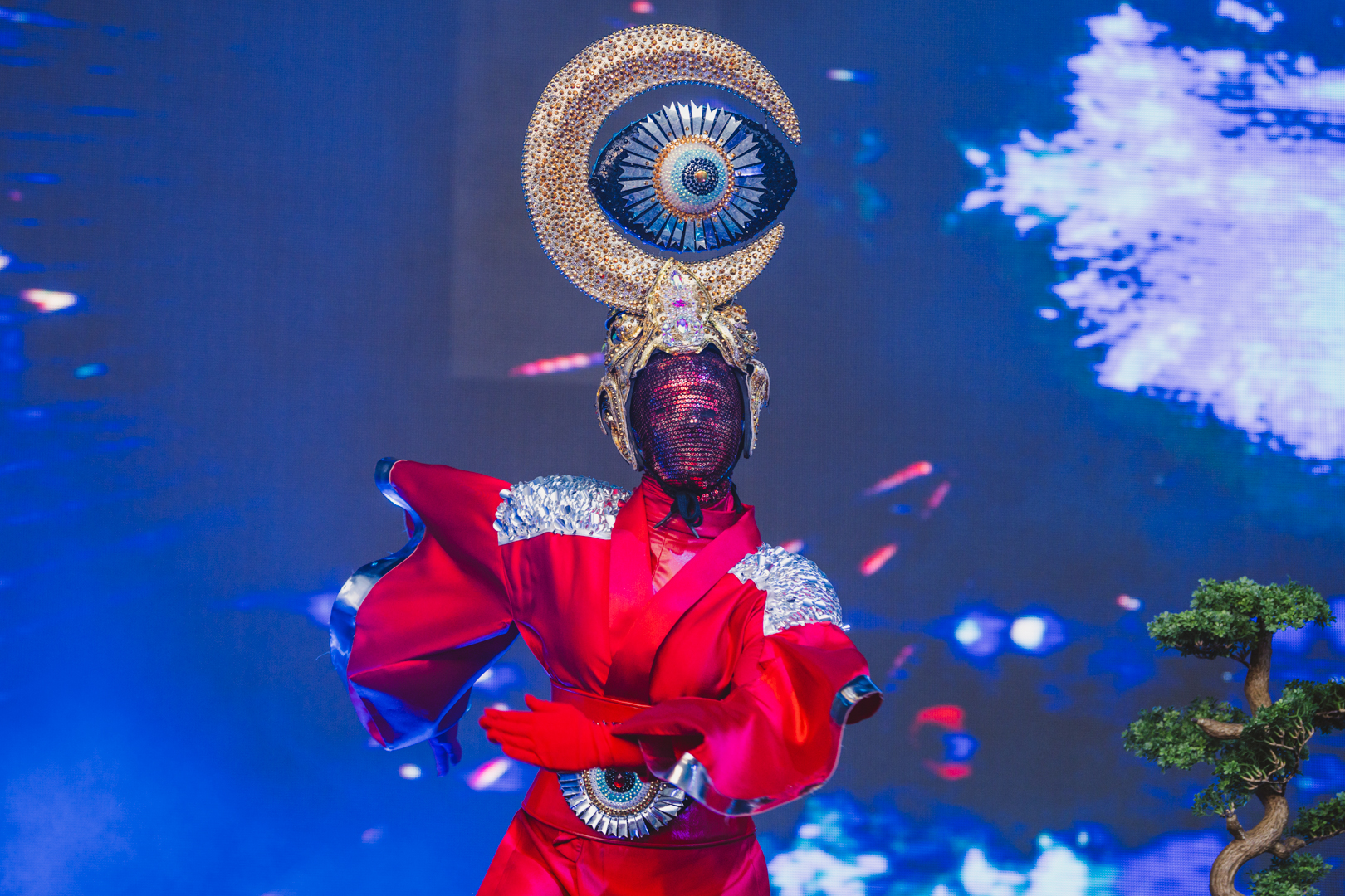Performer in ornate red costume with moon-shaped headpiece