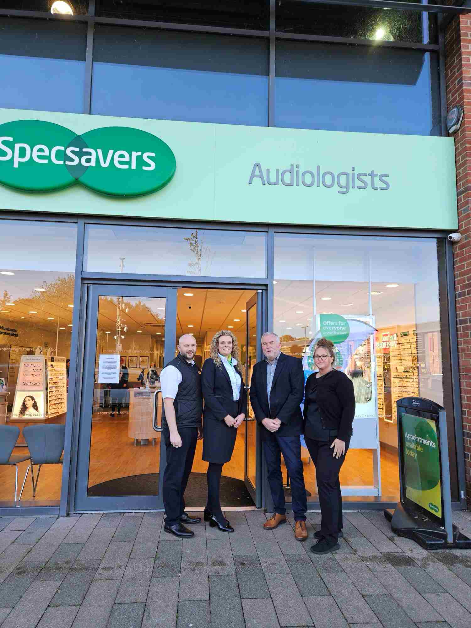 Four people standing outside Specsavers audiologists shop