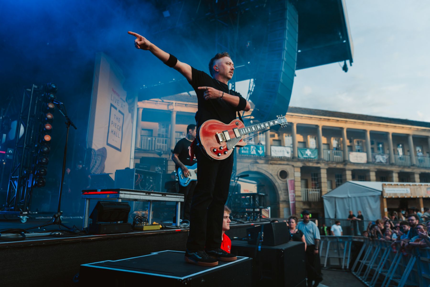 Guitarist on stage pointing at crowd with historic building backdrop