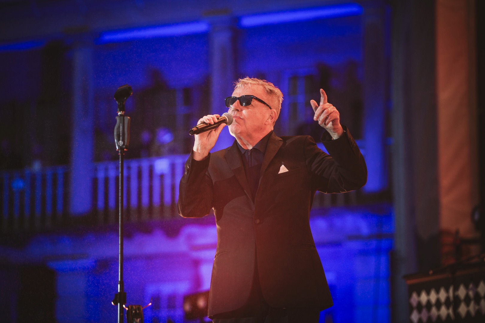 Singer in sunglasses performing on stage with blue lighting