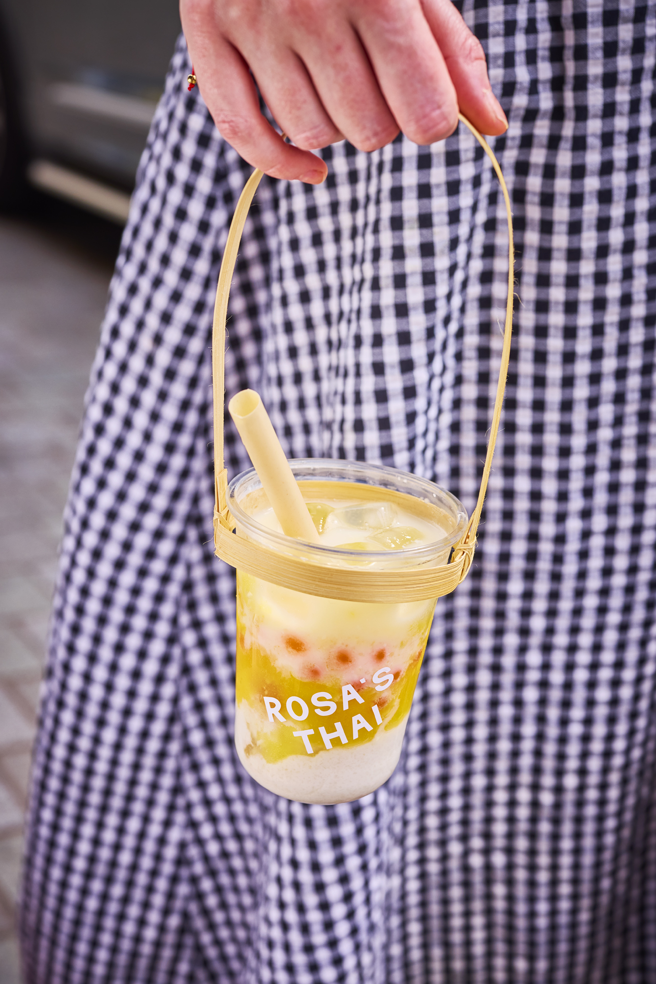 Hand holding a bamboo carrier with a Rosa's Thai bubble tea