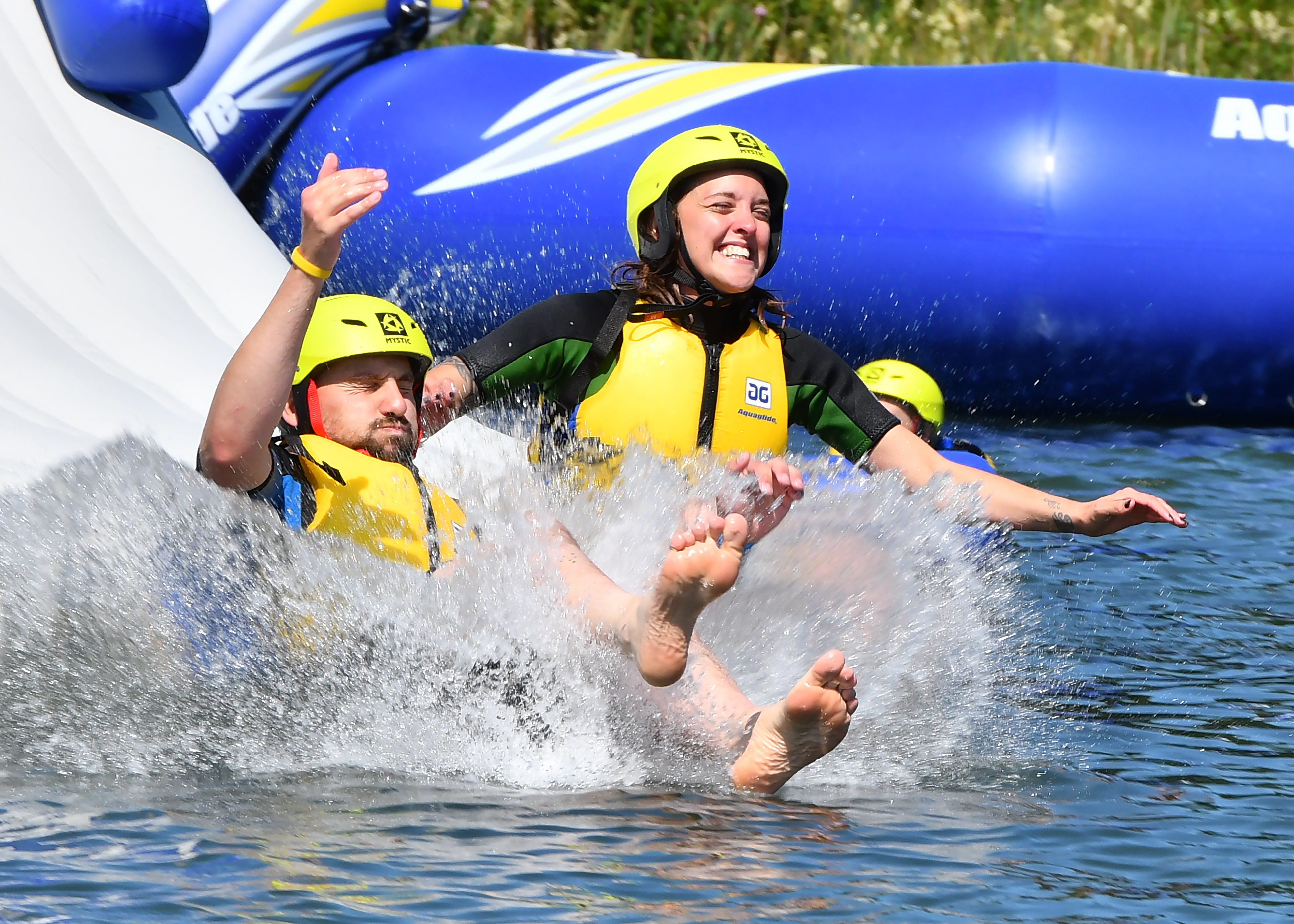 Two people in yellow life vests splash down water slide