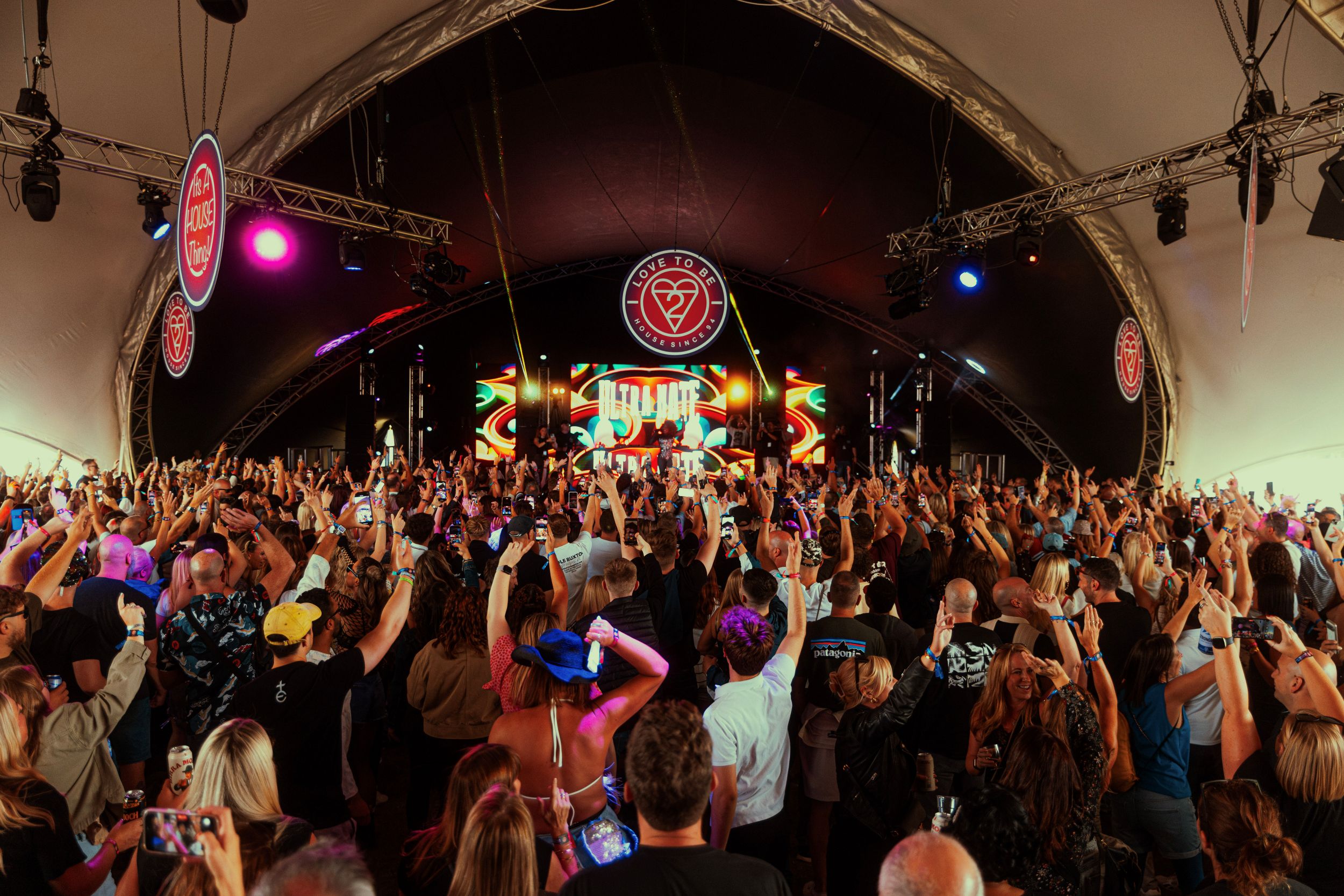 Crowd dancing under large tent with colorful stage lights