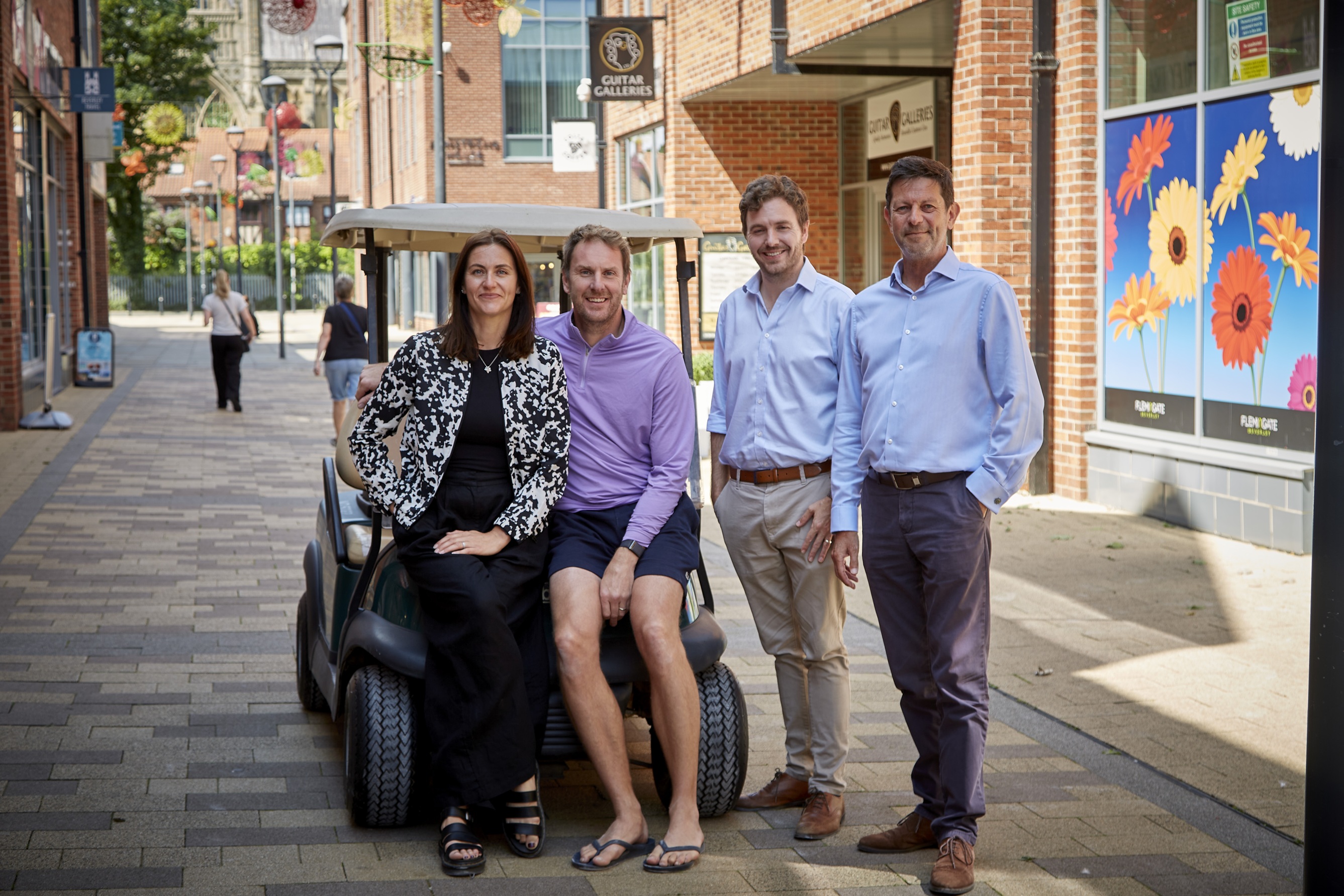 Four people posing with a golf cart on a sunny brick street