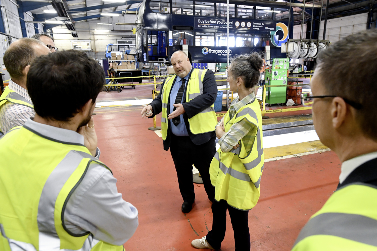 Group of people in high-vis jackets touring a bus depot