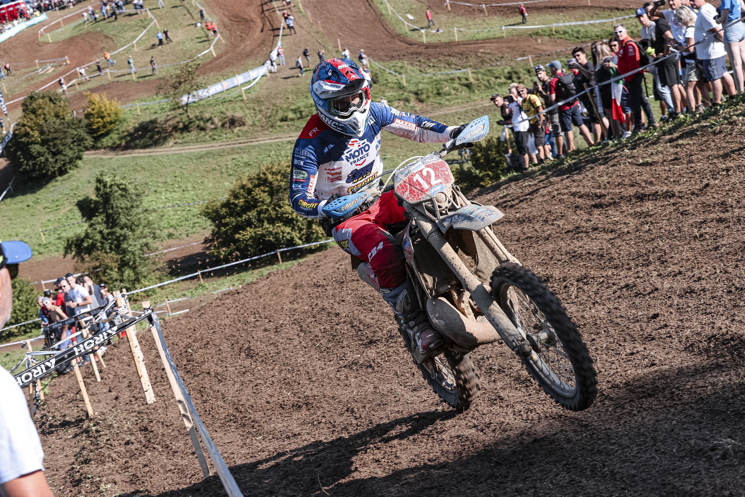 Motorcyclist in blue gear racing on muddy track with spectators