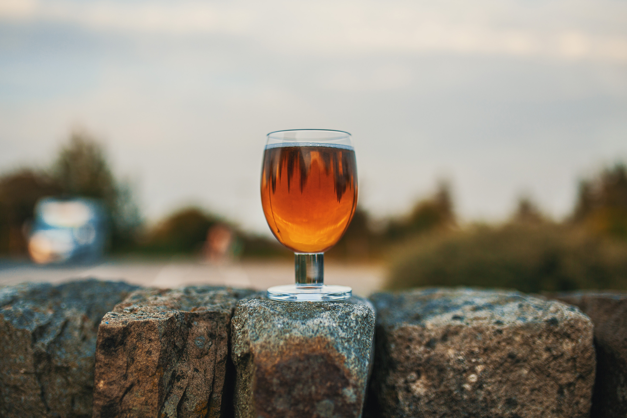 Glass of amber ale on a stone wall with blurred countryside