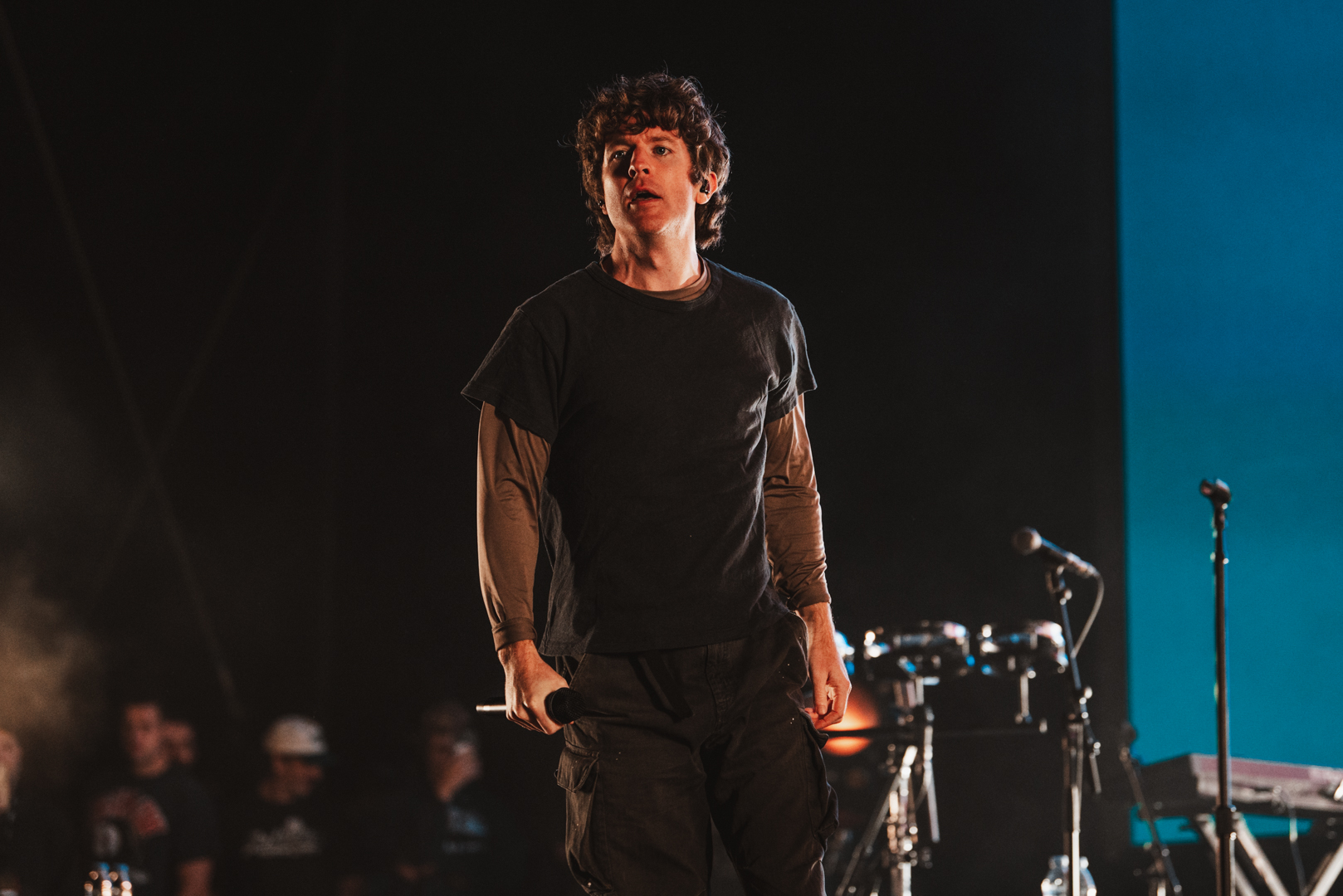 Musician performing on stage with dark backdrop and audience