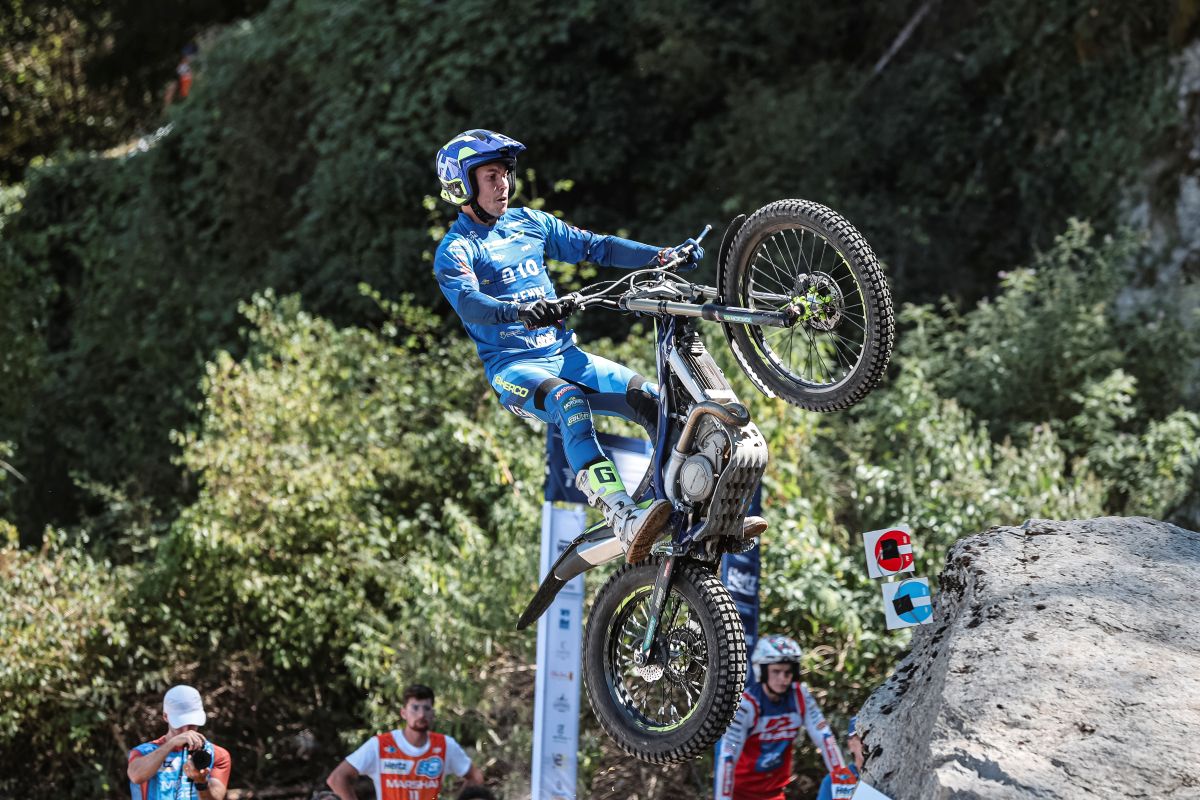 Motorcyclist in blue gear performing stunt on rocky hill