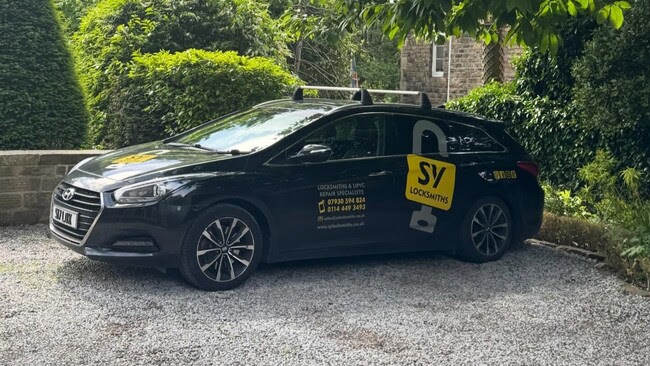 Black locksmith van parked on gravel driveway under trees