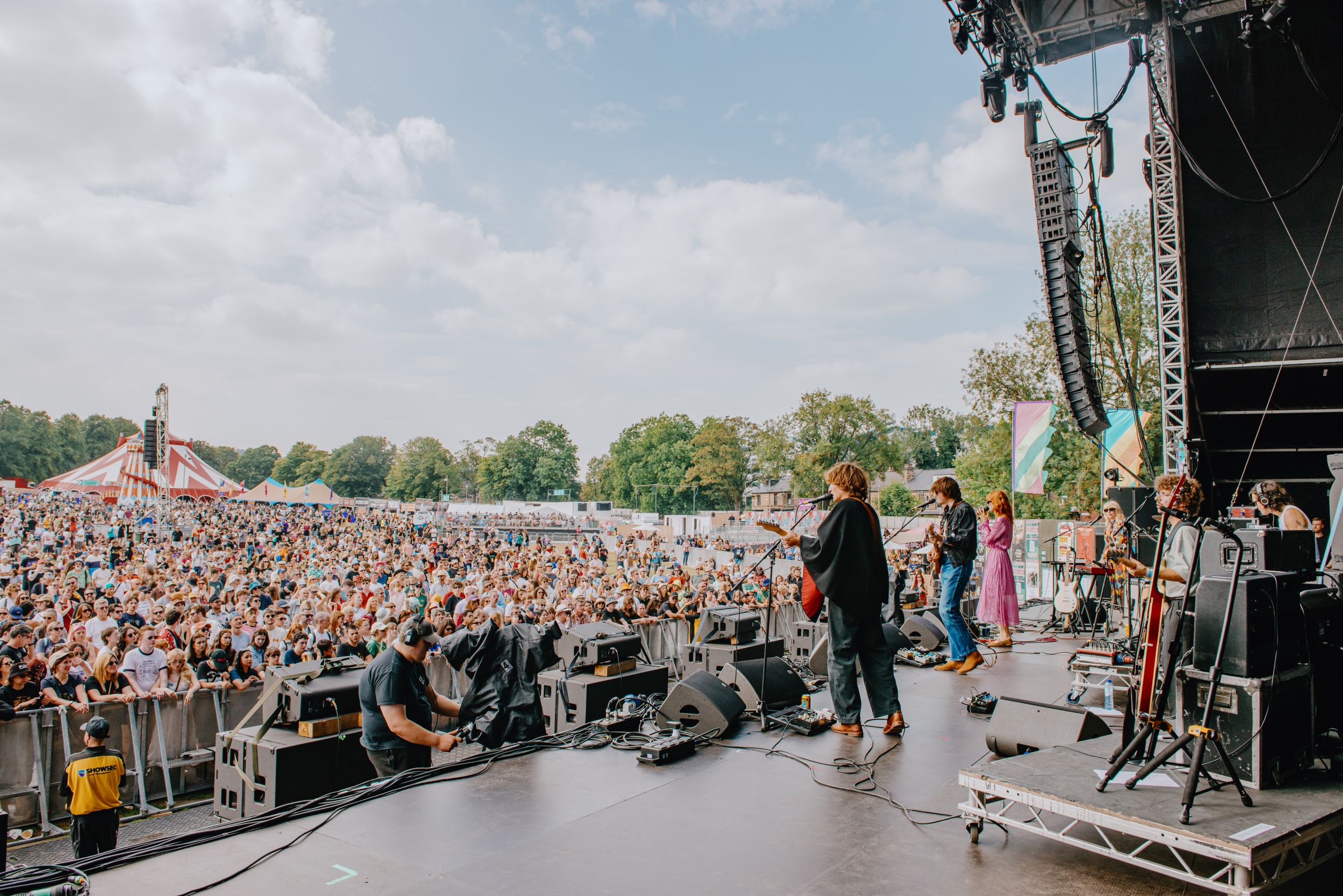 Festival crowd enjoying live band on outdoor stage with trees