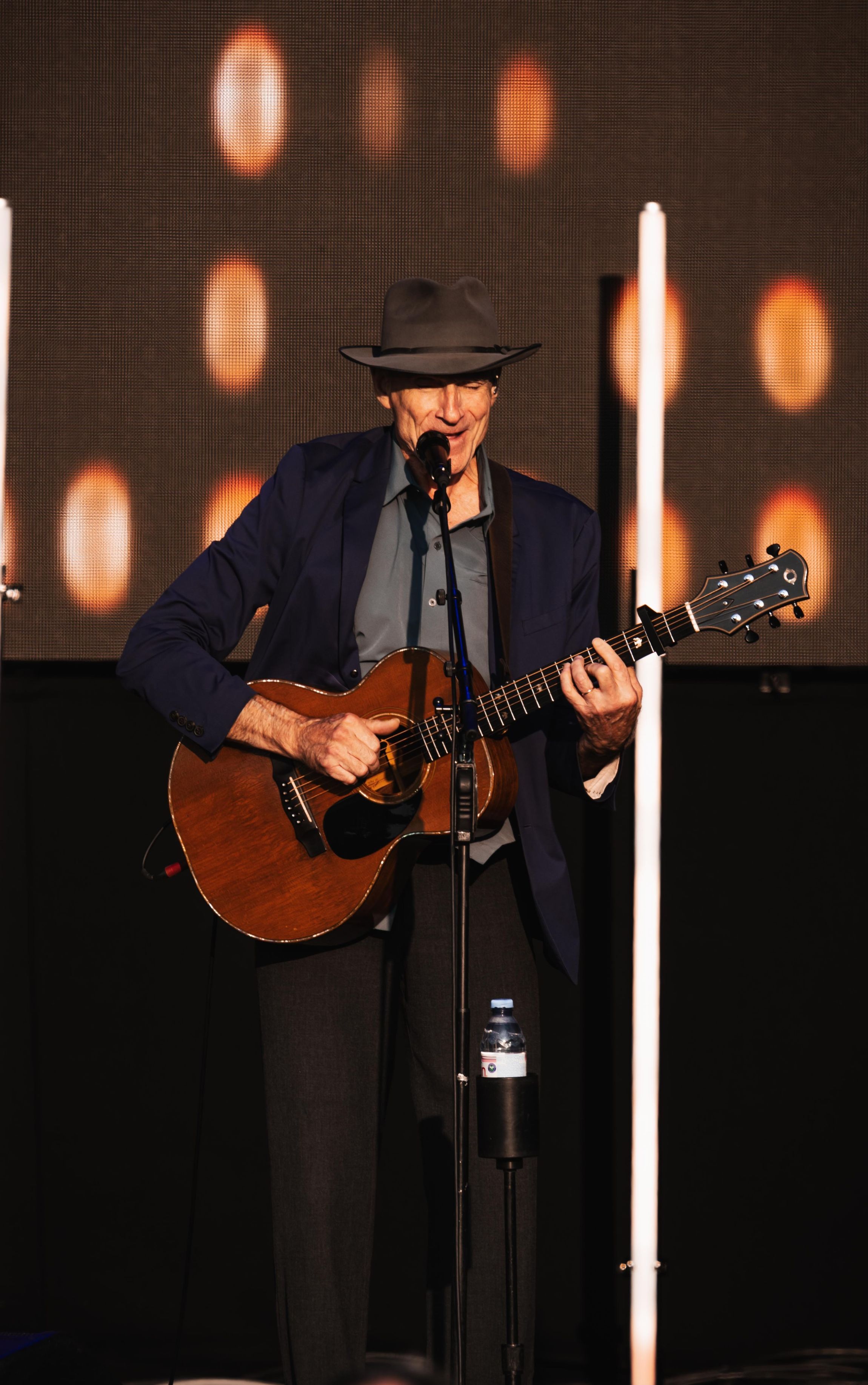 Elderly musician in grey hat playing acoustic guitar on stage