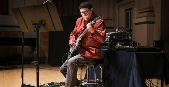 Elderly musician playing electric guitar on stage in a hall