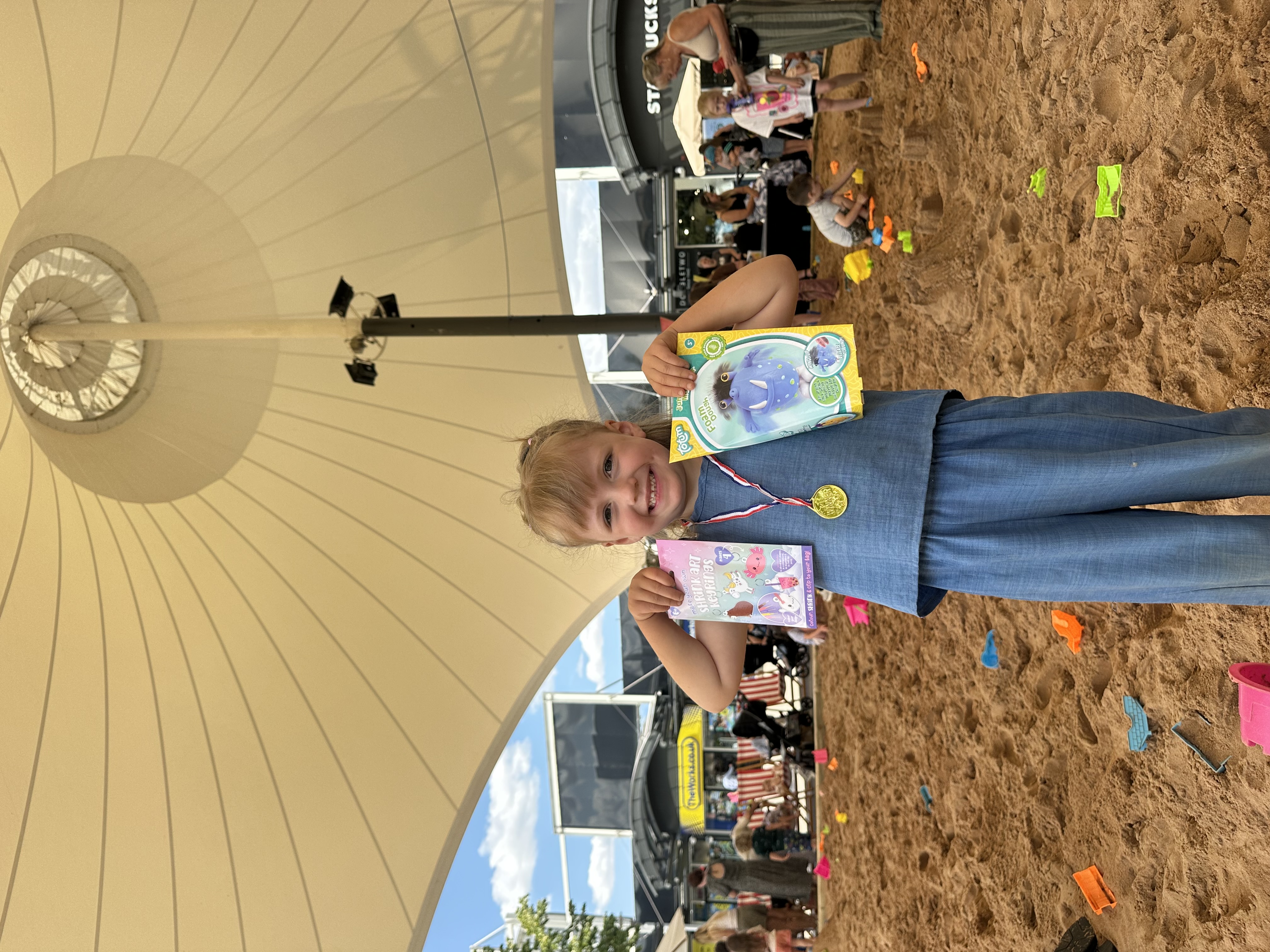 Smiling child holding toys under large white canopy on sand