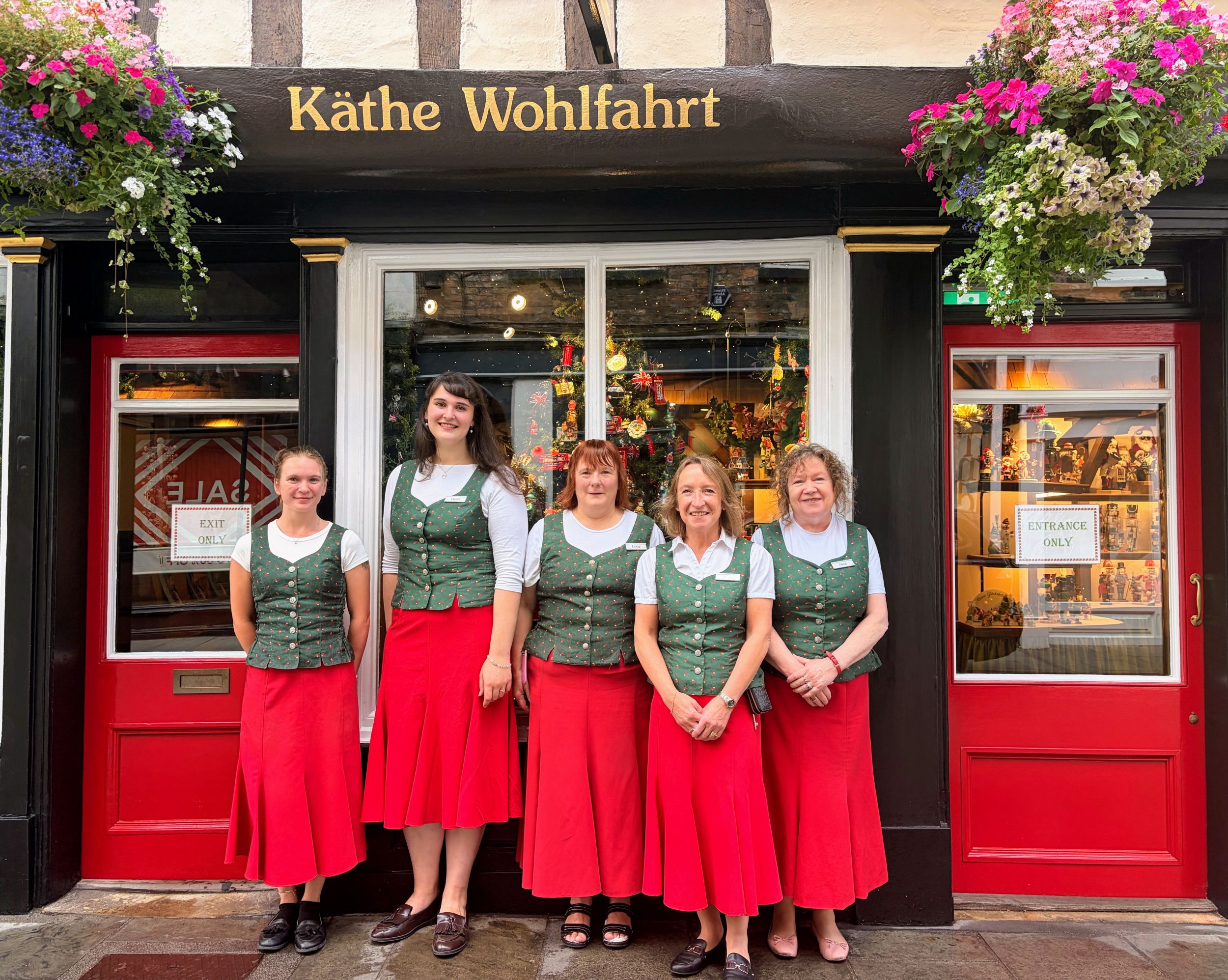 Five women in traditional attire outside a shop with red doors